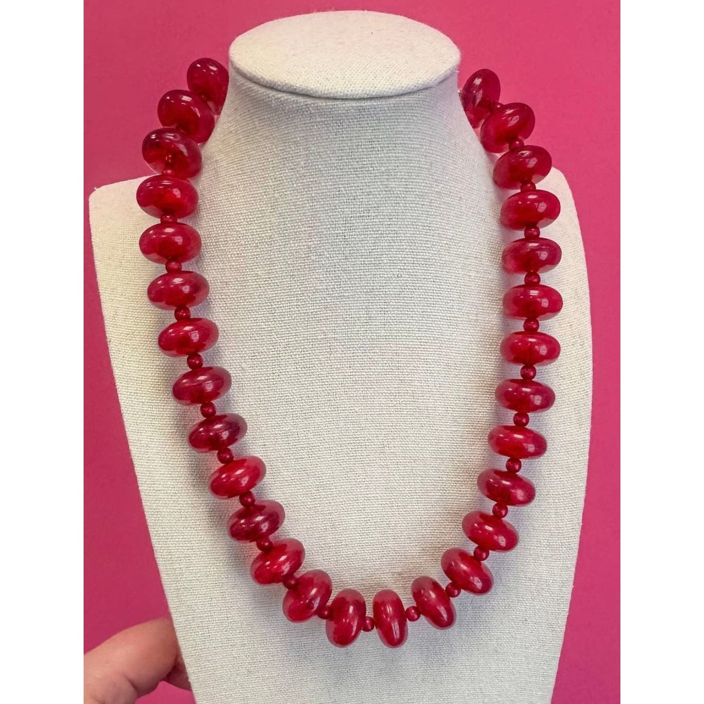 Red beaded necklace on a mannequin bust against a pink background