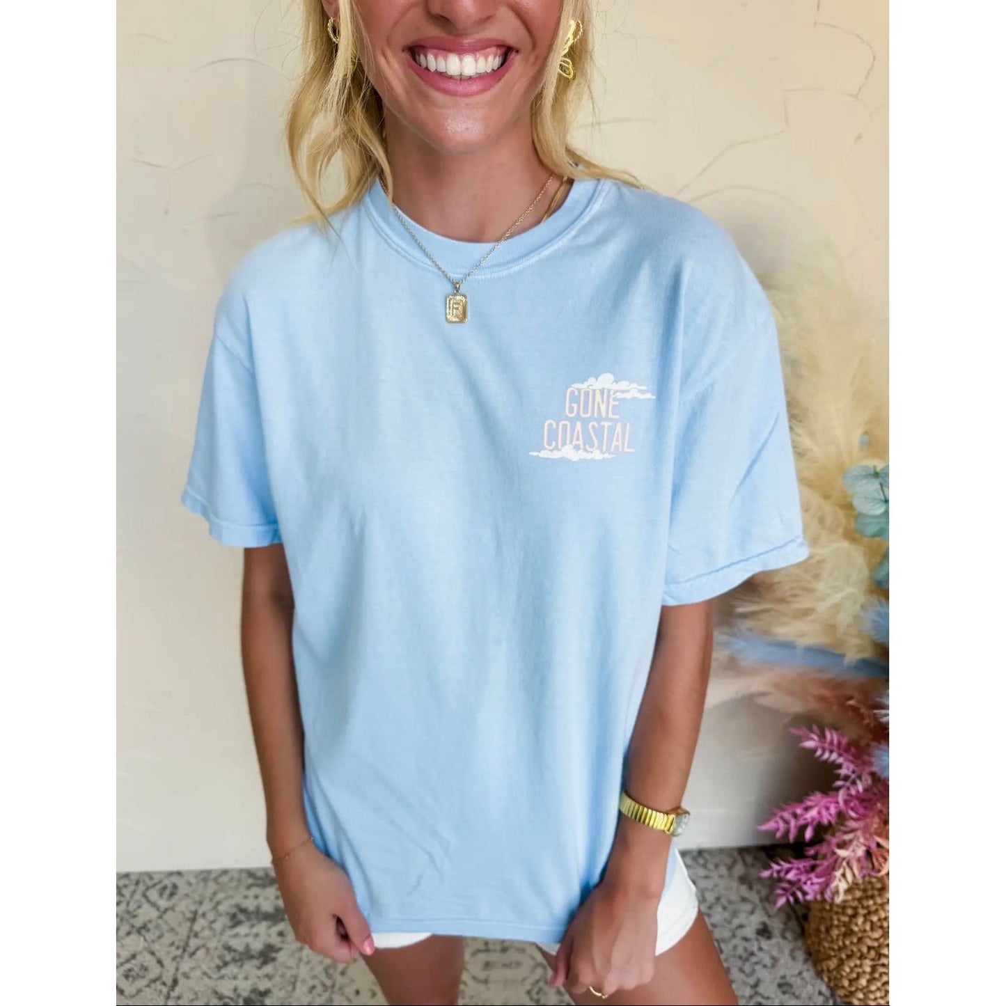 Woman wearing a light blue t-shirt with 'Coastal' text, smiling indoors.