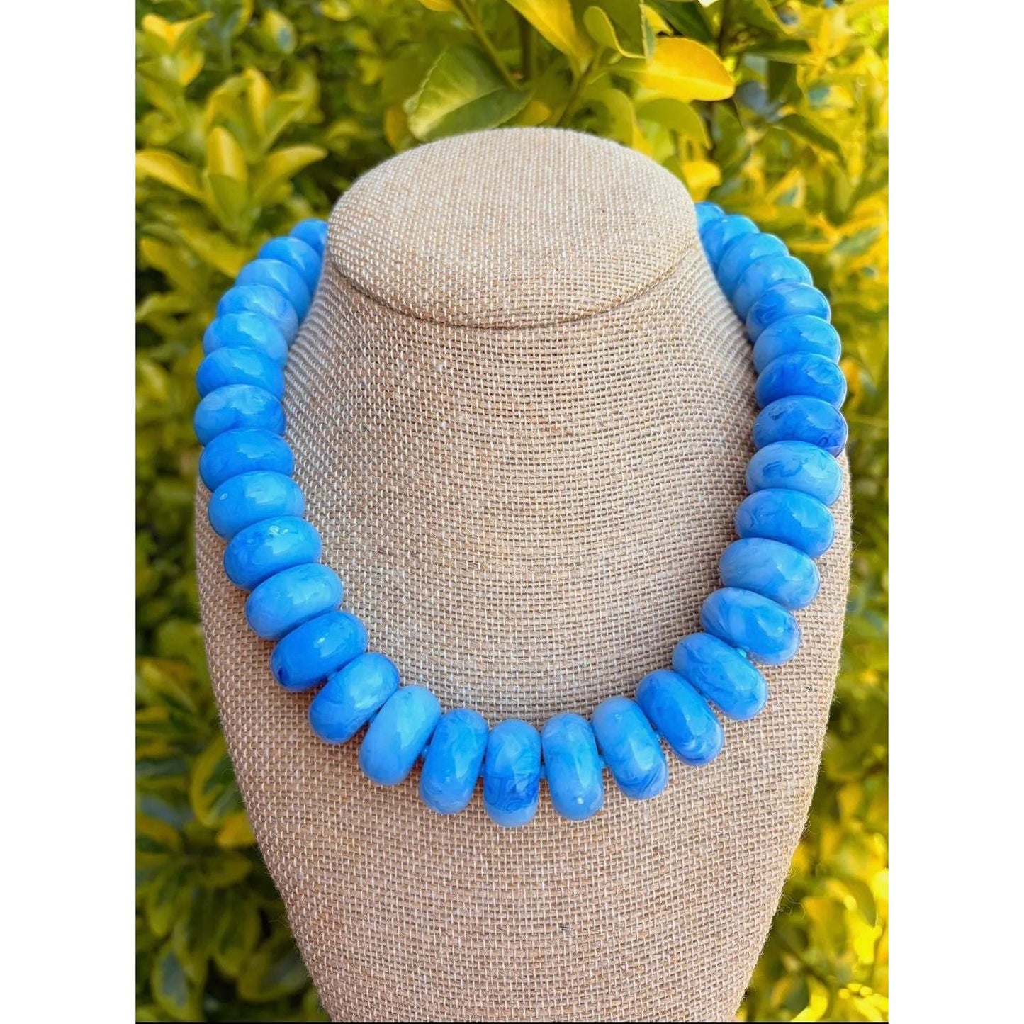 Blue beaded necklace on a mannequin bust with a green leafy background