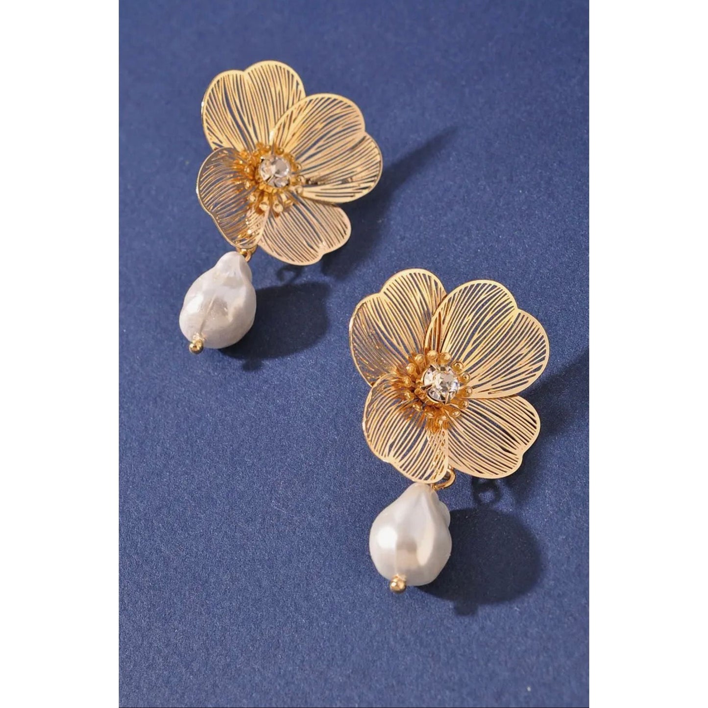 Gold floral earrings with pearl drops on a blue background