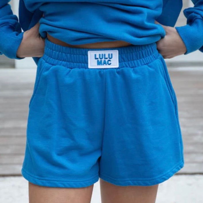 Person wearing blue shorts with a visible brand label, standing on a wooden deck.