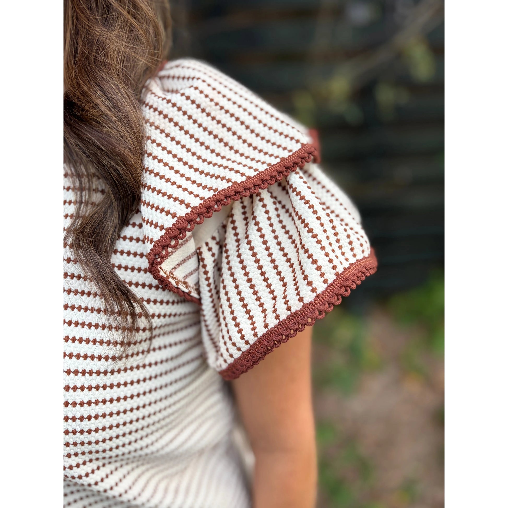 Close-up of a person wearing a white and brown patterned dress with a blurred natural background