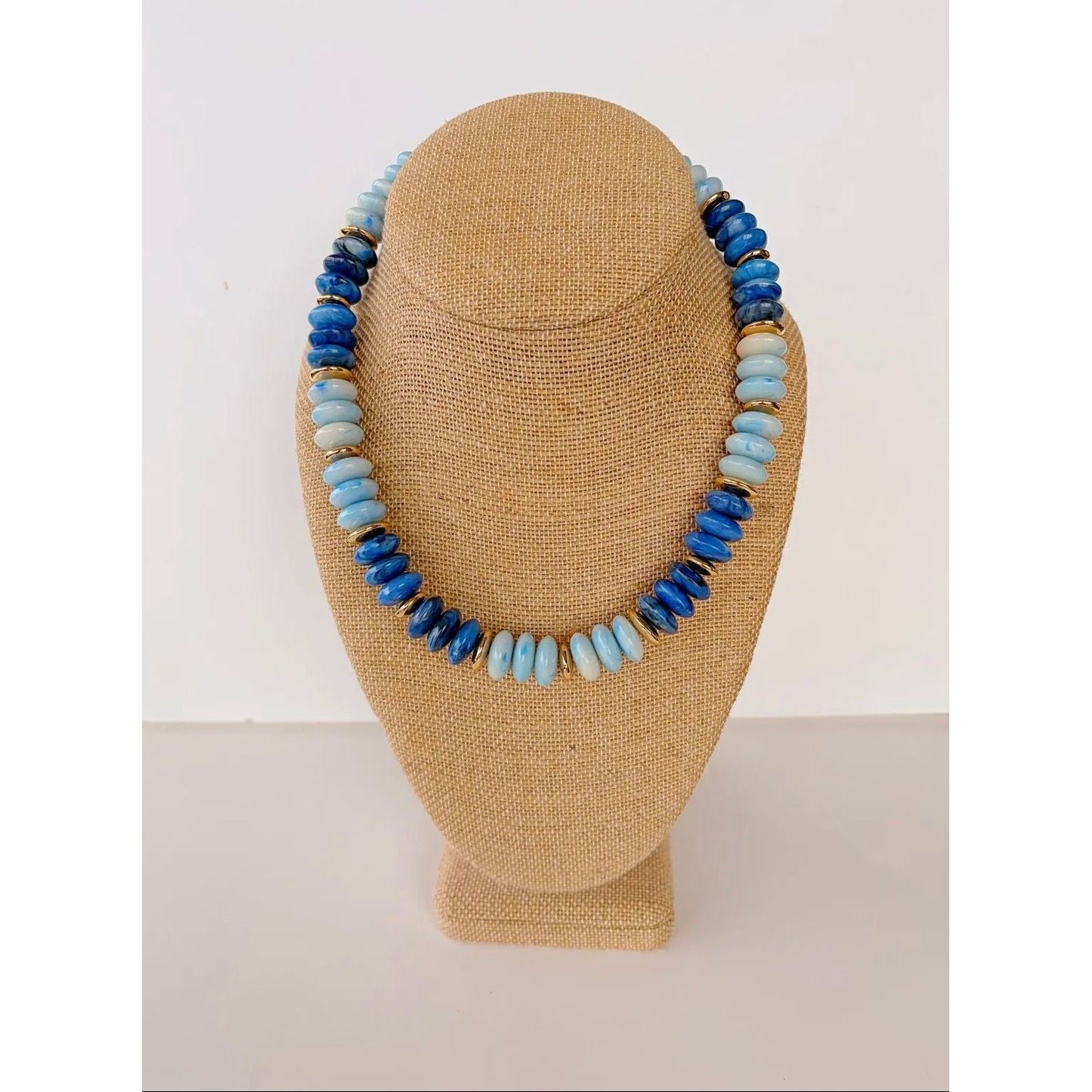 Necklace with blue and light blue beads on a tan mannequin bust against a white background