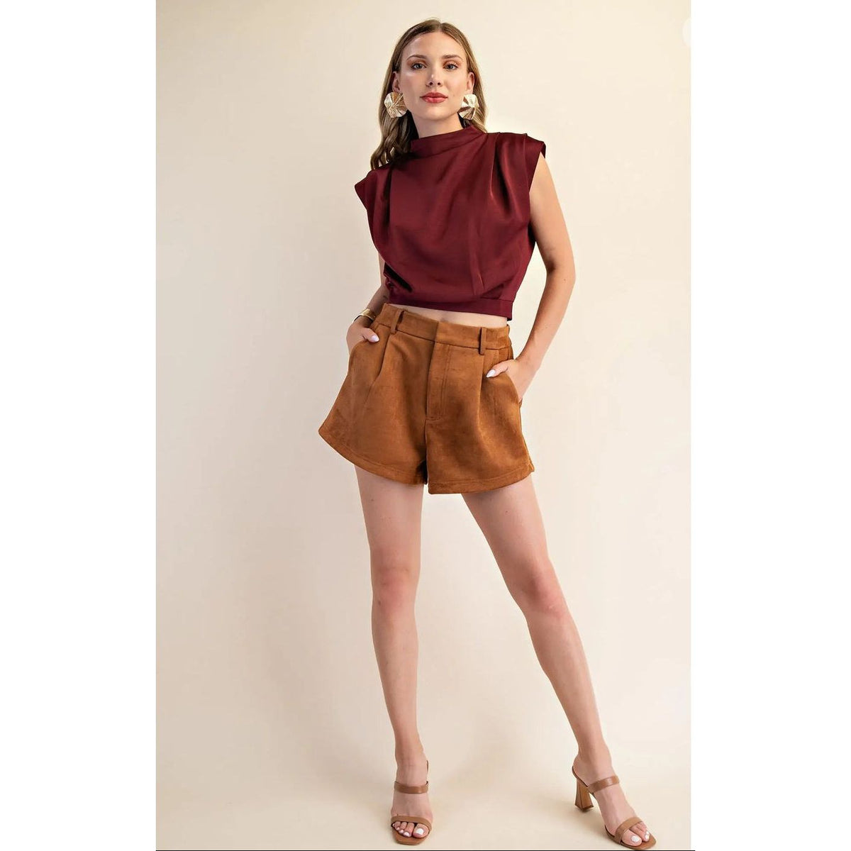 Woman wearing a burgundy top and brown shorts on a beige background