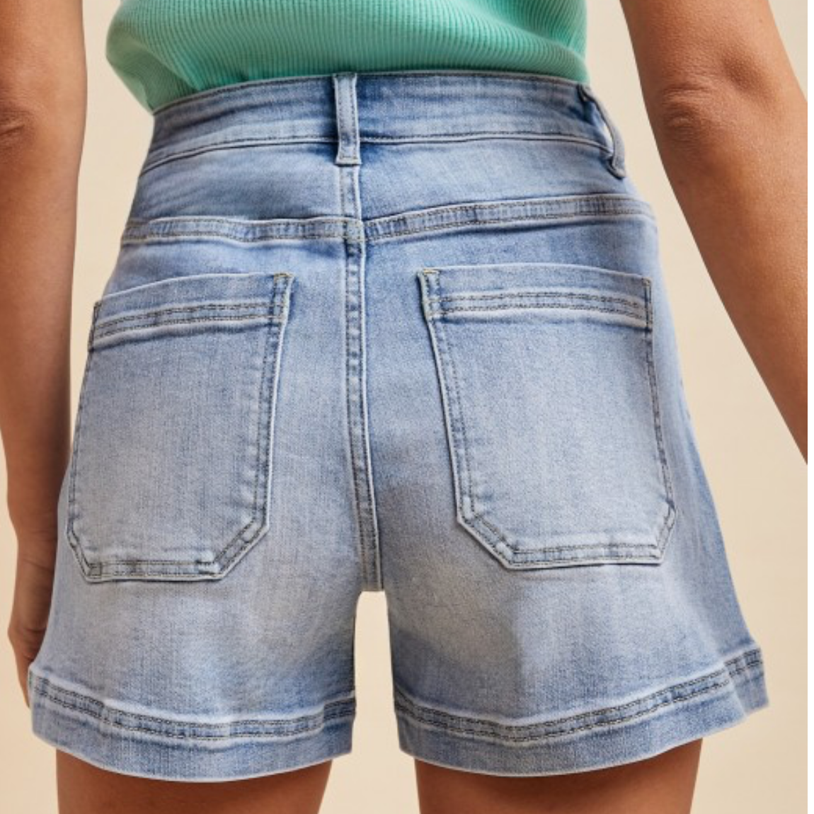 Denim shorts being worn on a person with a beige background, displayed on a shopping app.