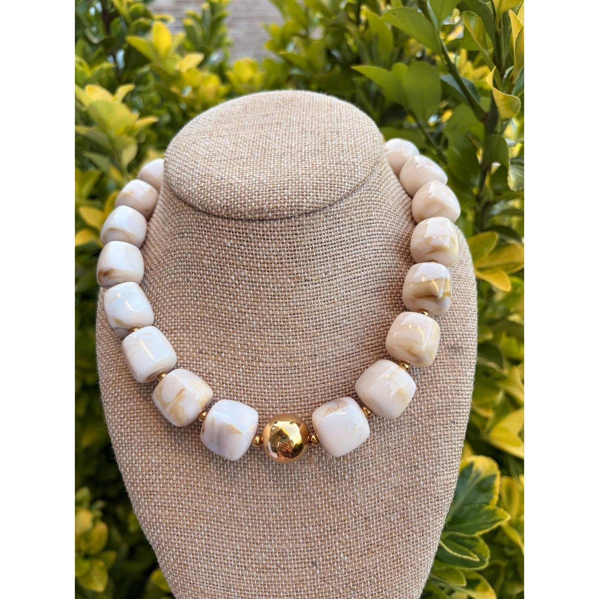 Annie Ks Boutique beige cube bead necklace featuring a polished gold ball centerpiece on a fabric display bust.