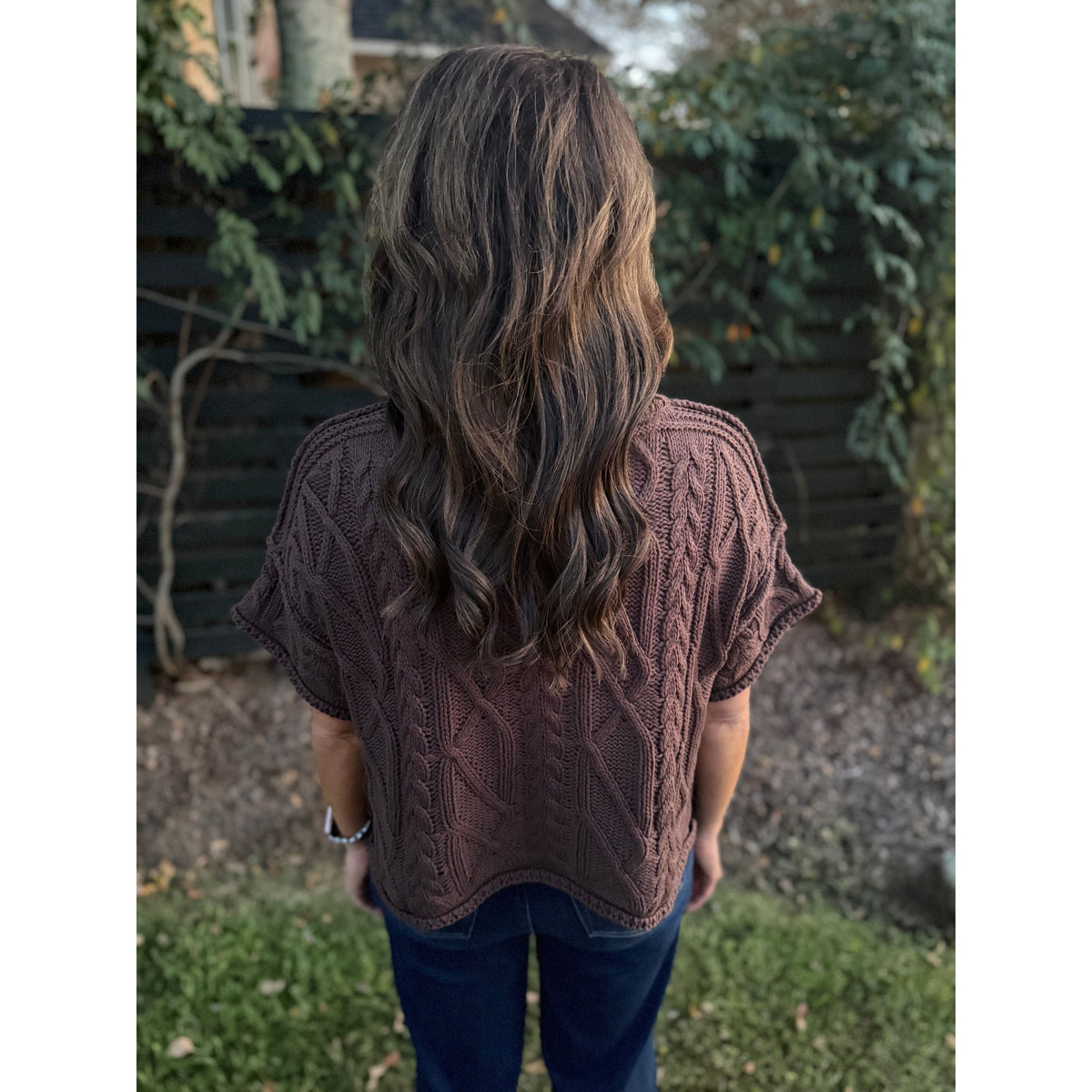Back view of Annie Ks Boutique brown short sleeve cropped knit sweater with cable knit texture worn with blue jeans