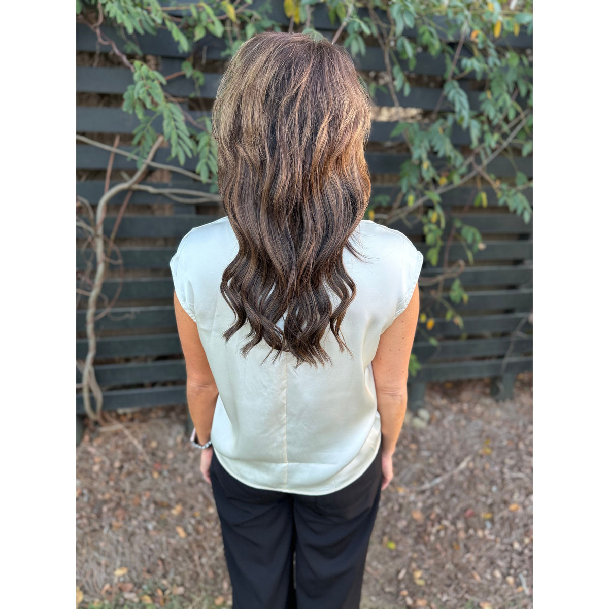 Annie Ks Boutique champagne sleeveless satin top worn by a woman with long wavy hair, back view