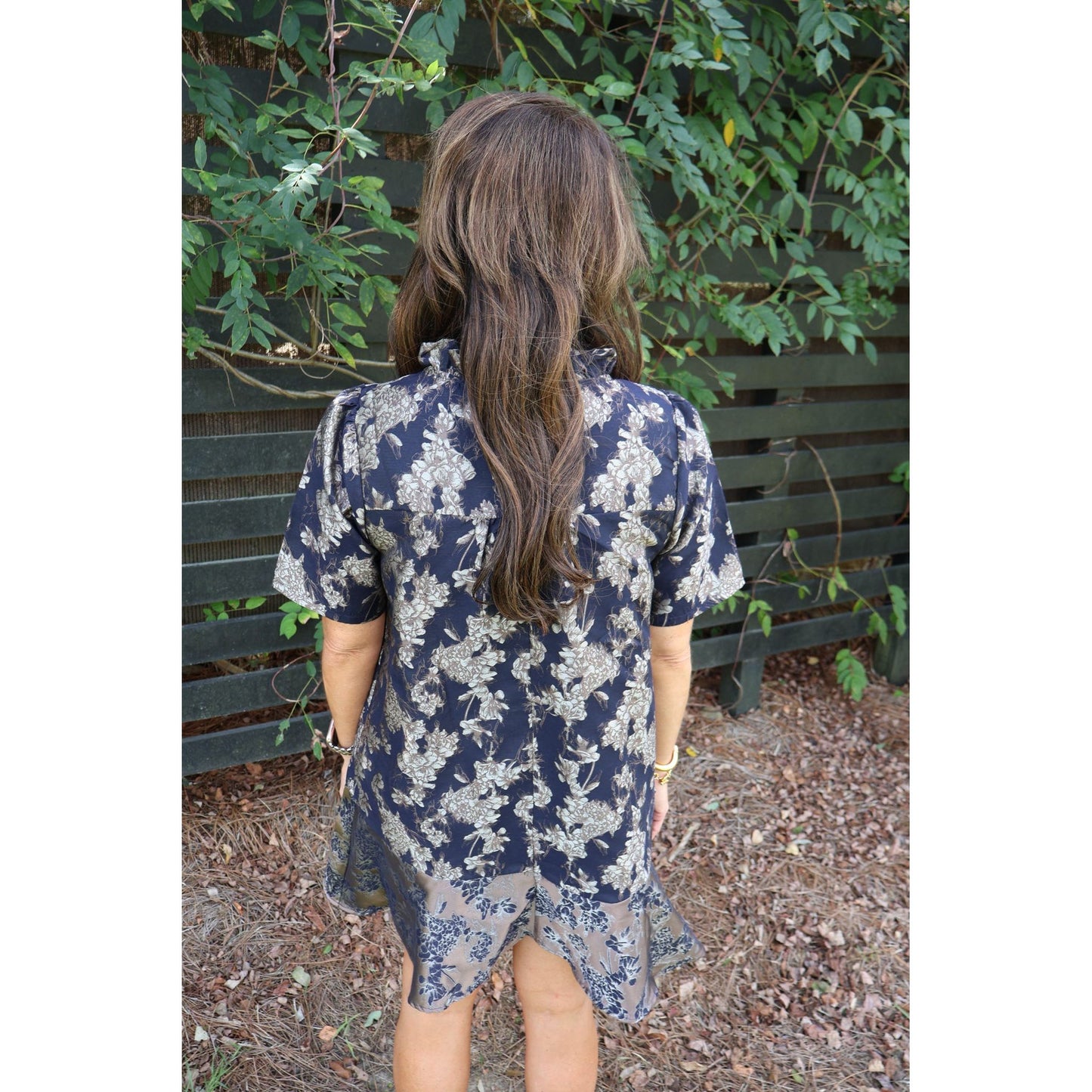 Annie Ks Boutique navy floral jacquard dress with ruffle neckline and flounce hem seen from the back on a model