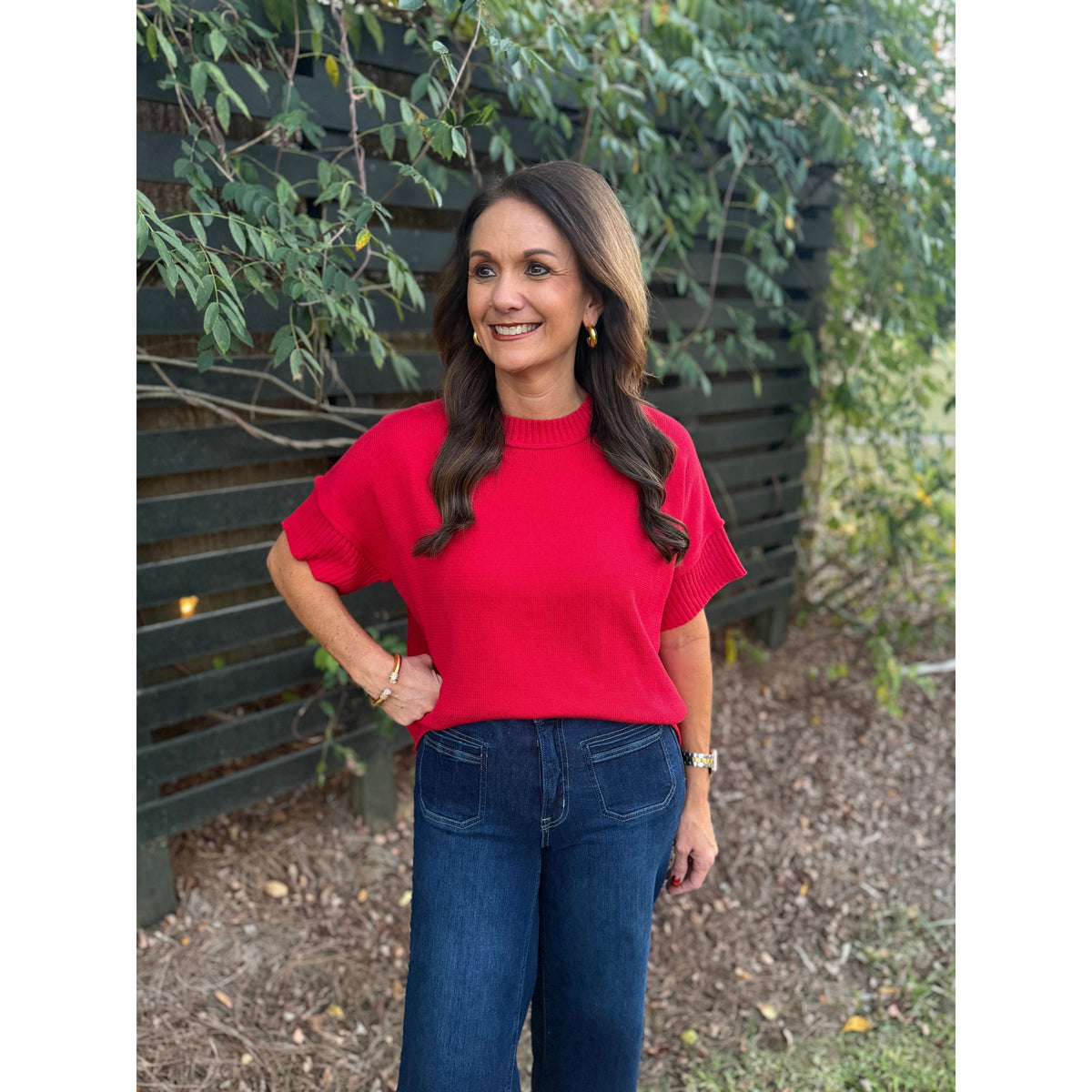 Annie Ks Boutique red crew neck sweater with drop shoulder half sleeves worn with dark wash denim jeans outdoors.