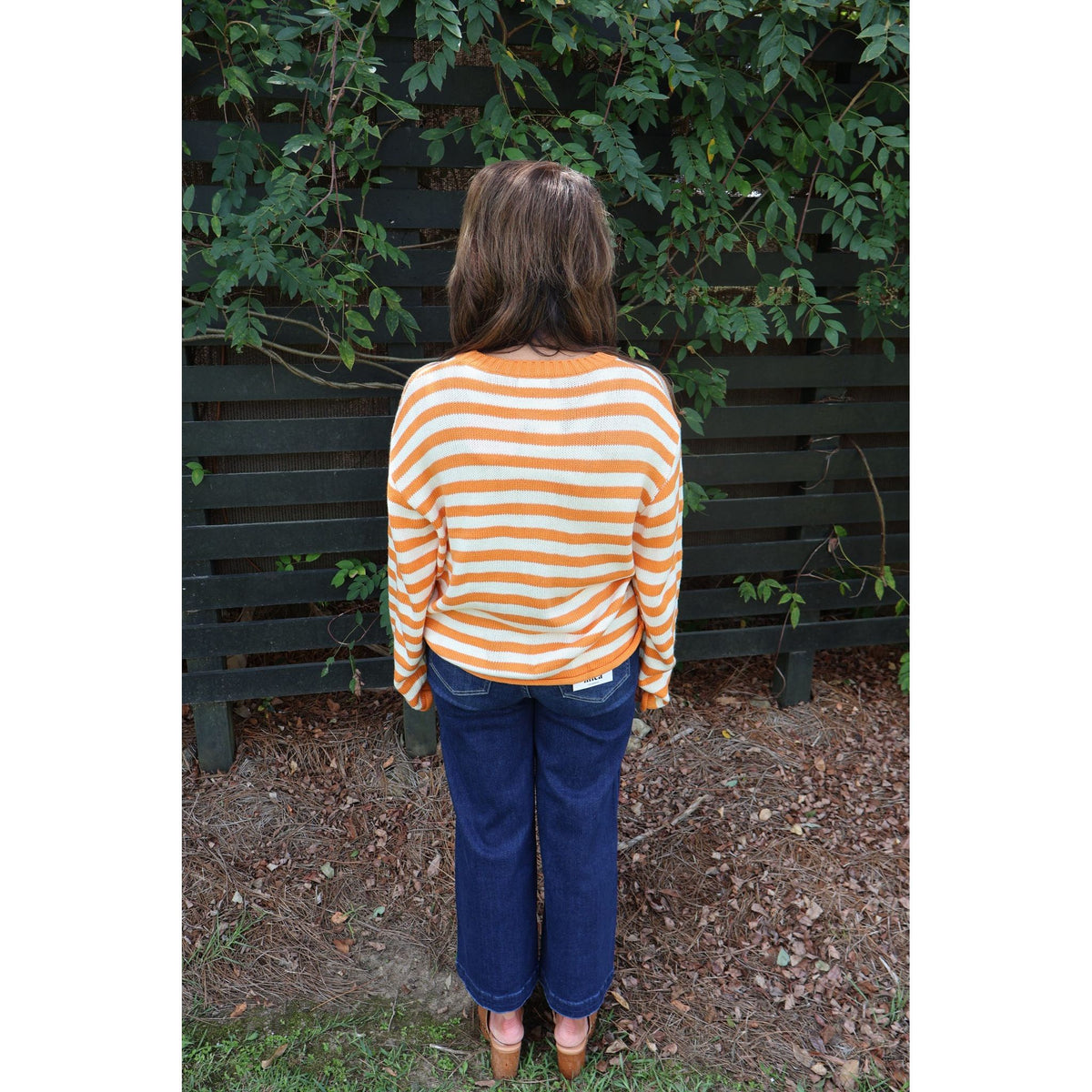Annie Ks Boutique orange and ivory striped crewneck knit sweater worn by a woman with dark jeans, back view