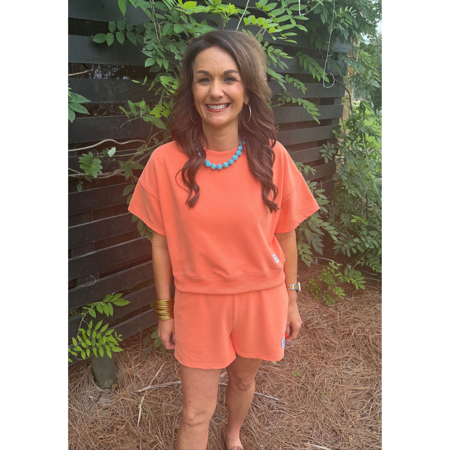 Annie Ks Boutique Watermelon Sugar short set in sun-kissed coral cotton blend worn by a smiling woman outdoors.