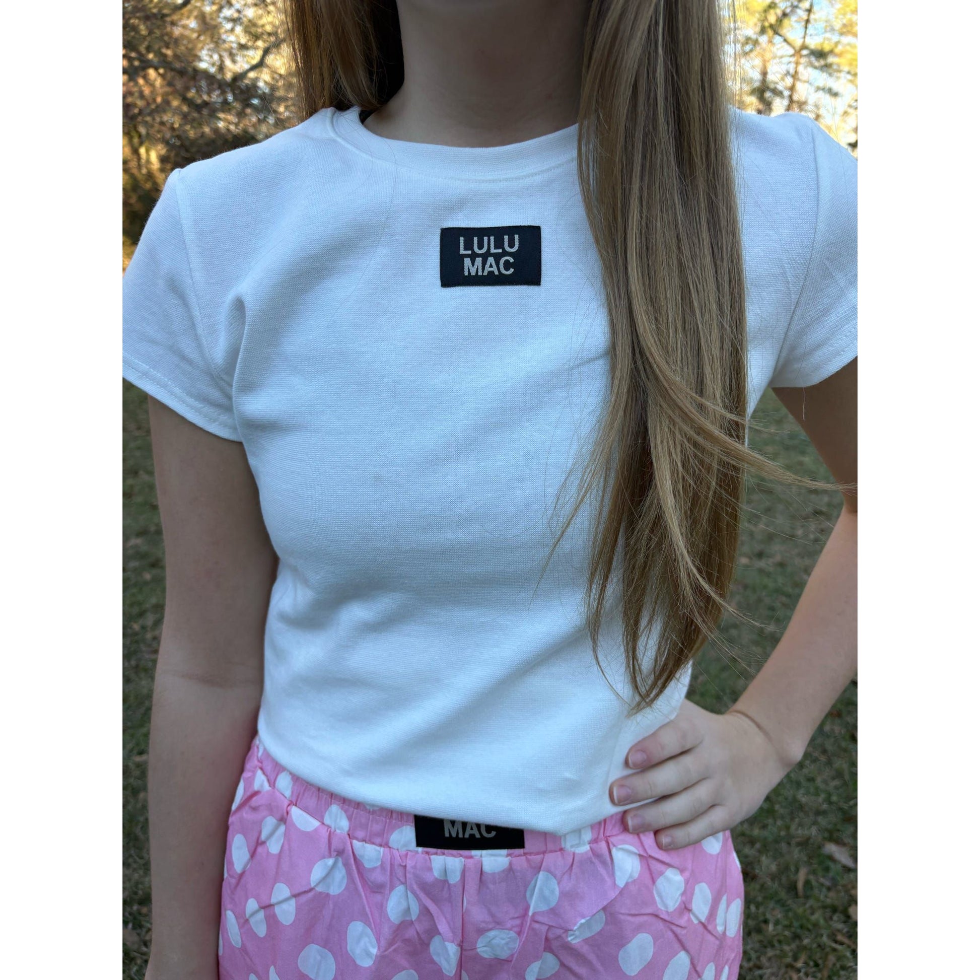 Person wearing a white t-shirt with 'Lulu Mac' branding outdoors.