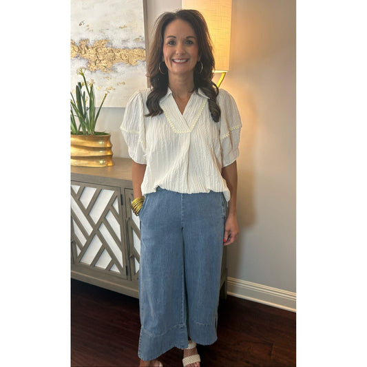 Woman in a white blouse and blue pants standing in a room with decorative elements.