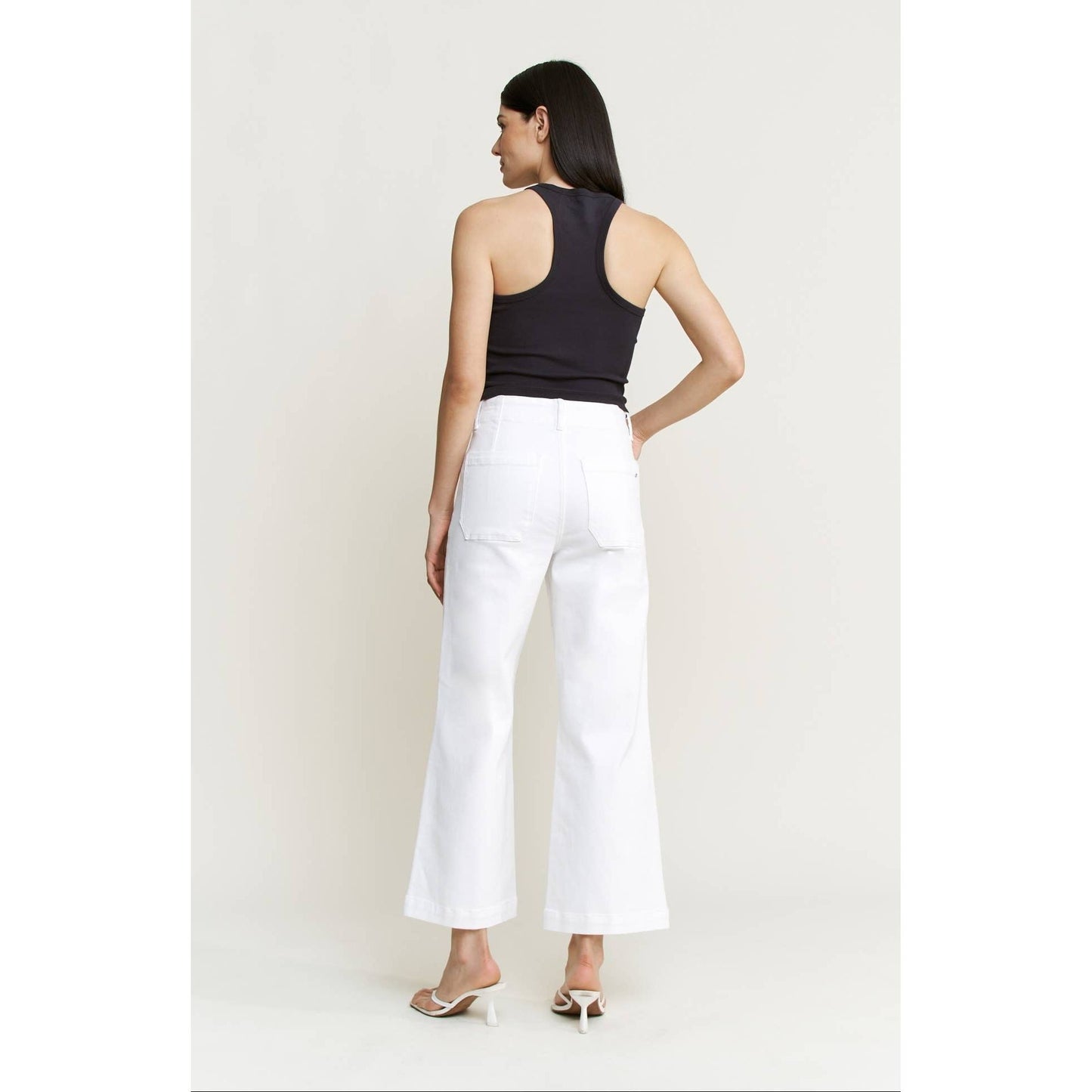 Woman wearing a black sleeveless top and white pants on a plain background