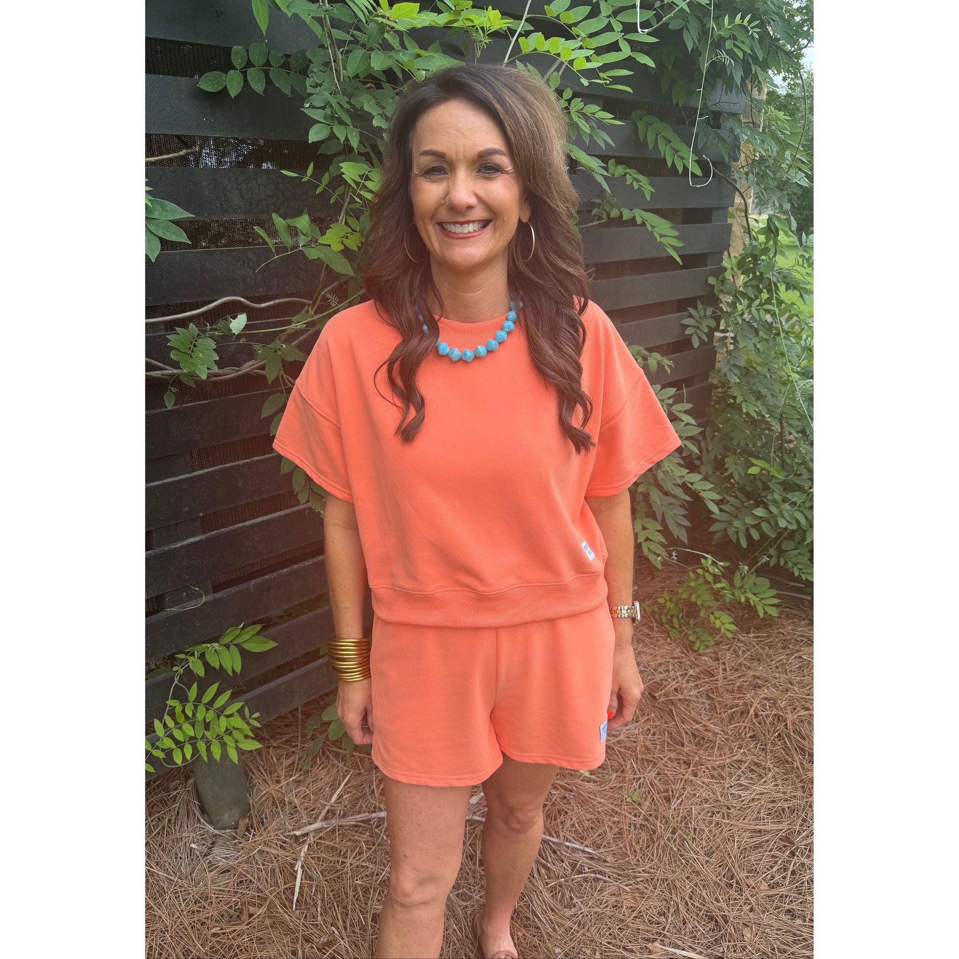 Woman wearing an orange dress standing outdoors with greenery around