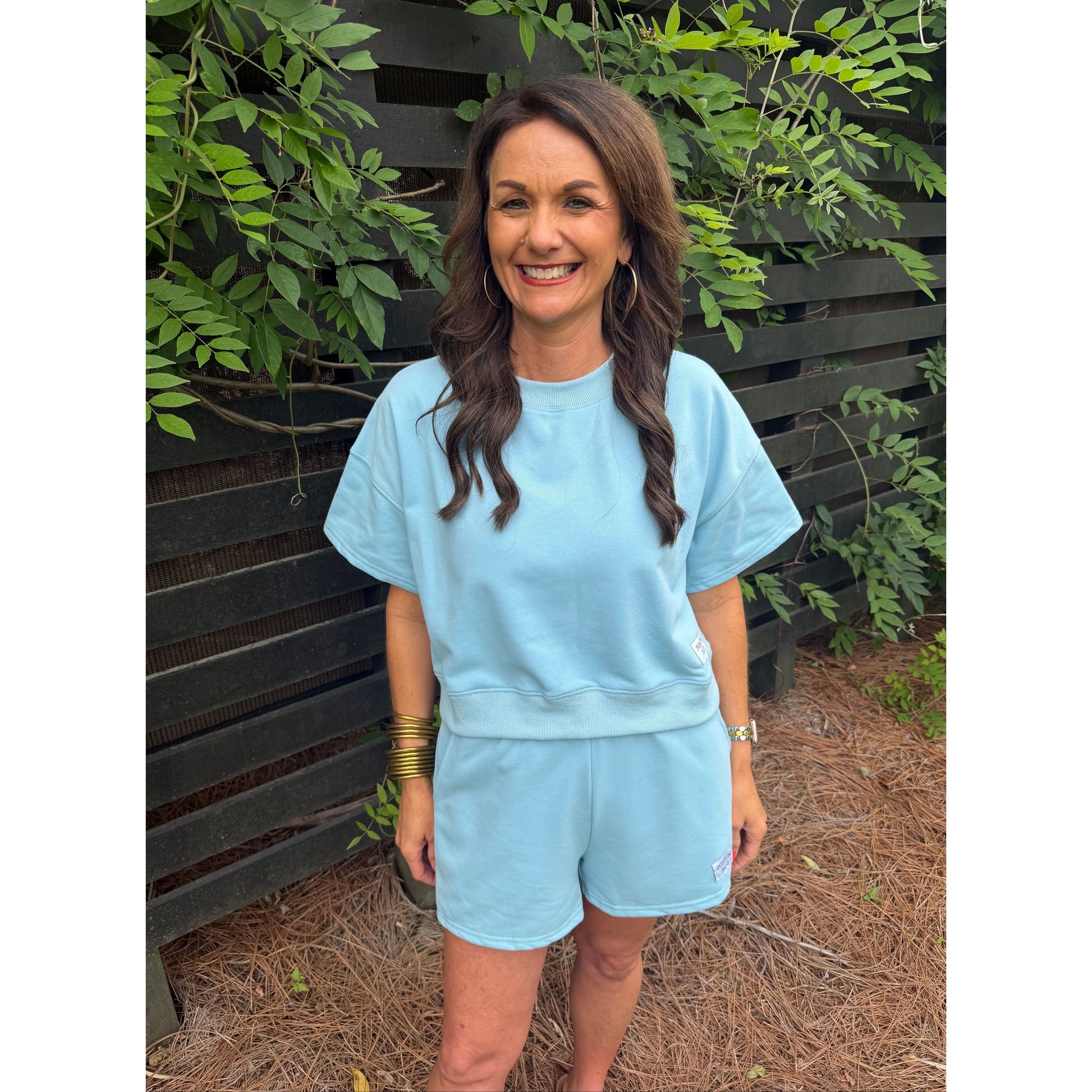 Person wearing a light blue dress standing outdoors with greenery around