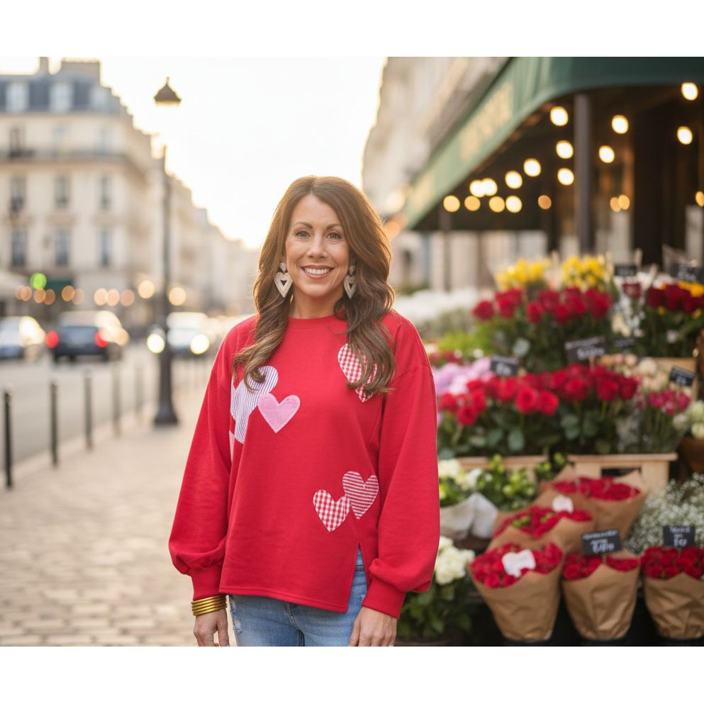 Woman wearing a red sweatshirt with heart designs standing outside a building.