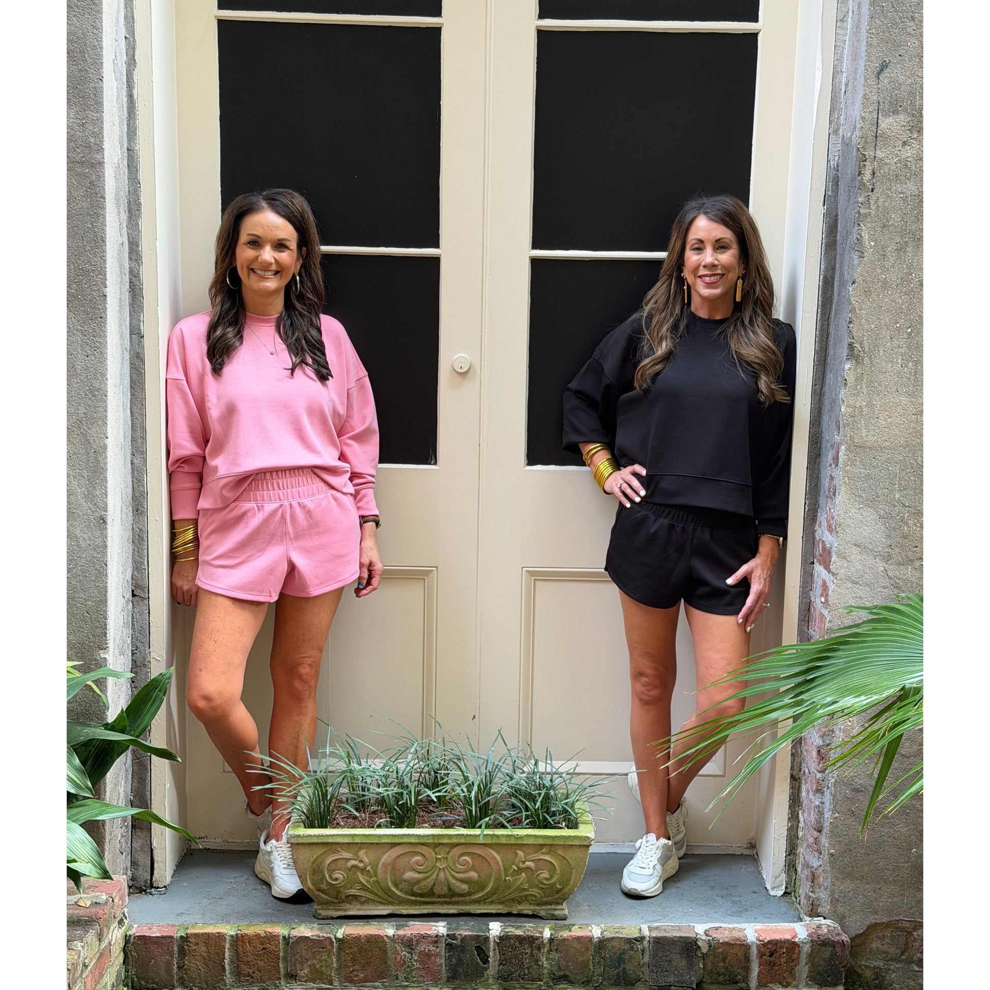 Two women standing in front of a door with plants around.