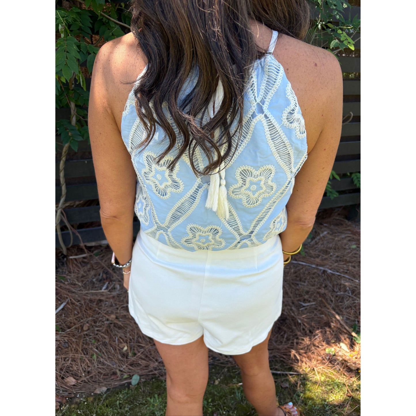 Person wearing a light blue lace top and white shorts outdoors.
