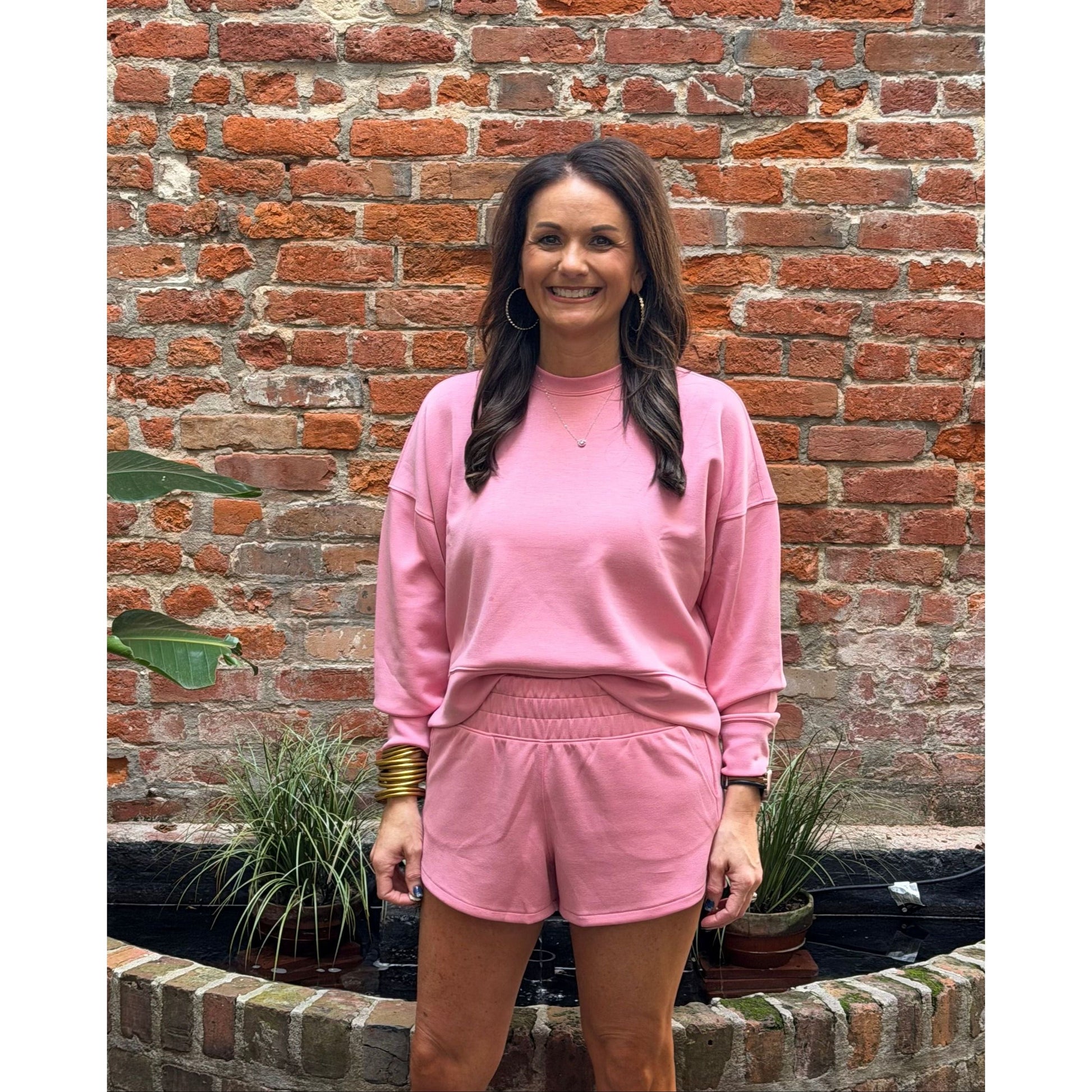 Woman in pink outfit standing in front of a brick wall