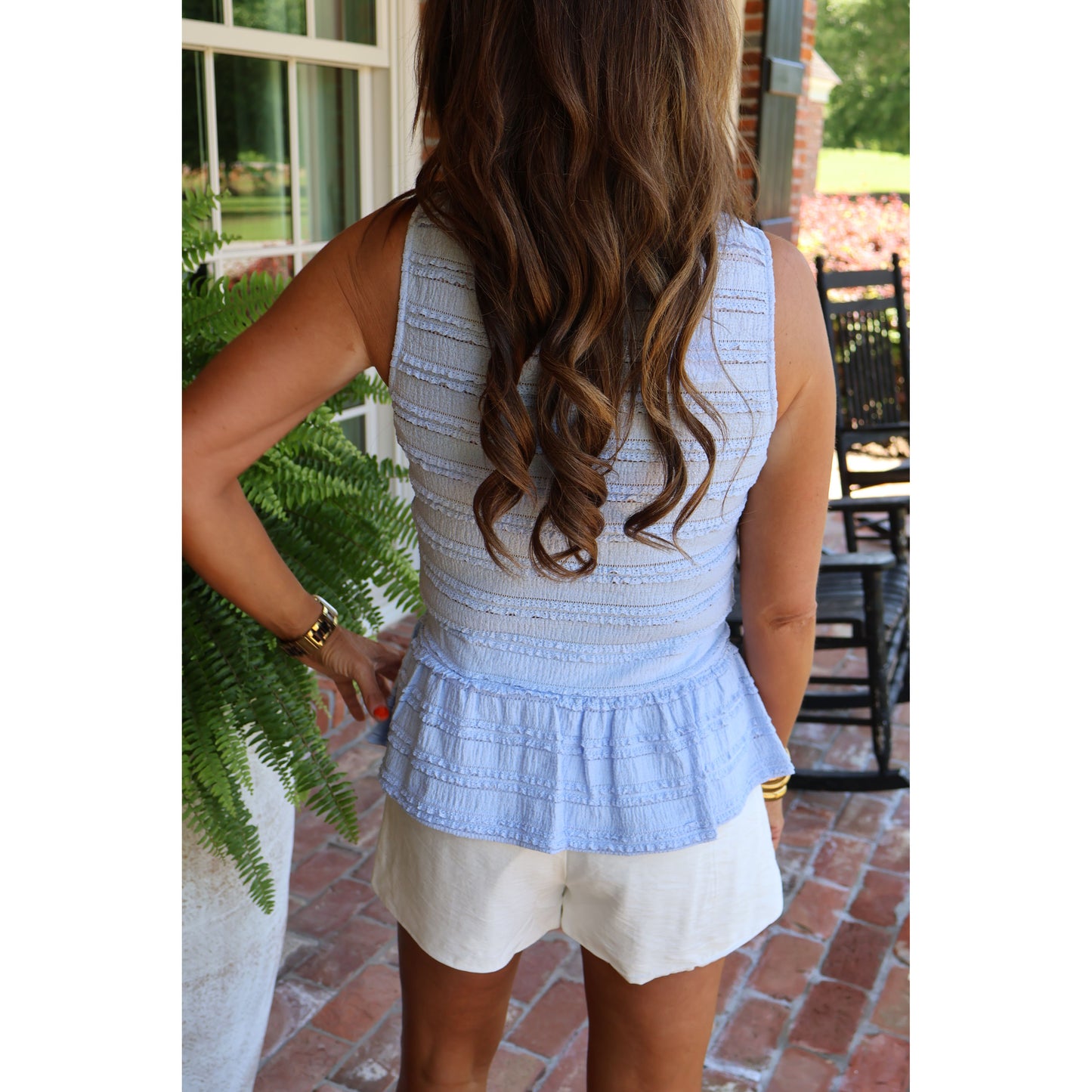 Woman wearing a light blue top and white shorts outdoors on a patio.