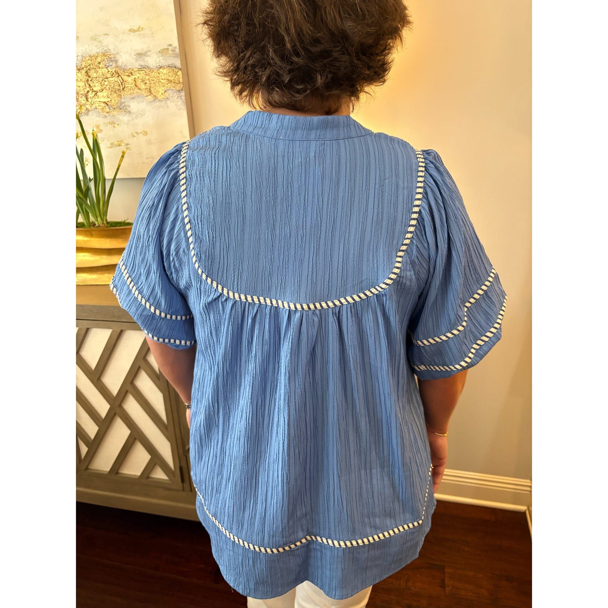 Person wearing a blue blouse with white trim in an indoor setting