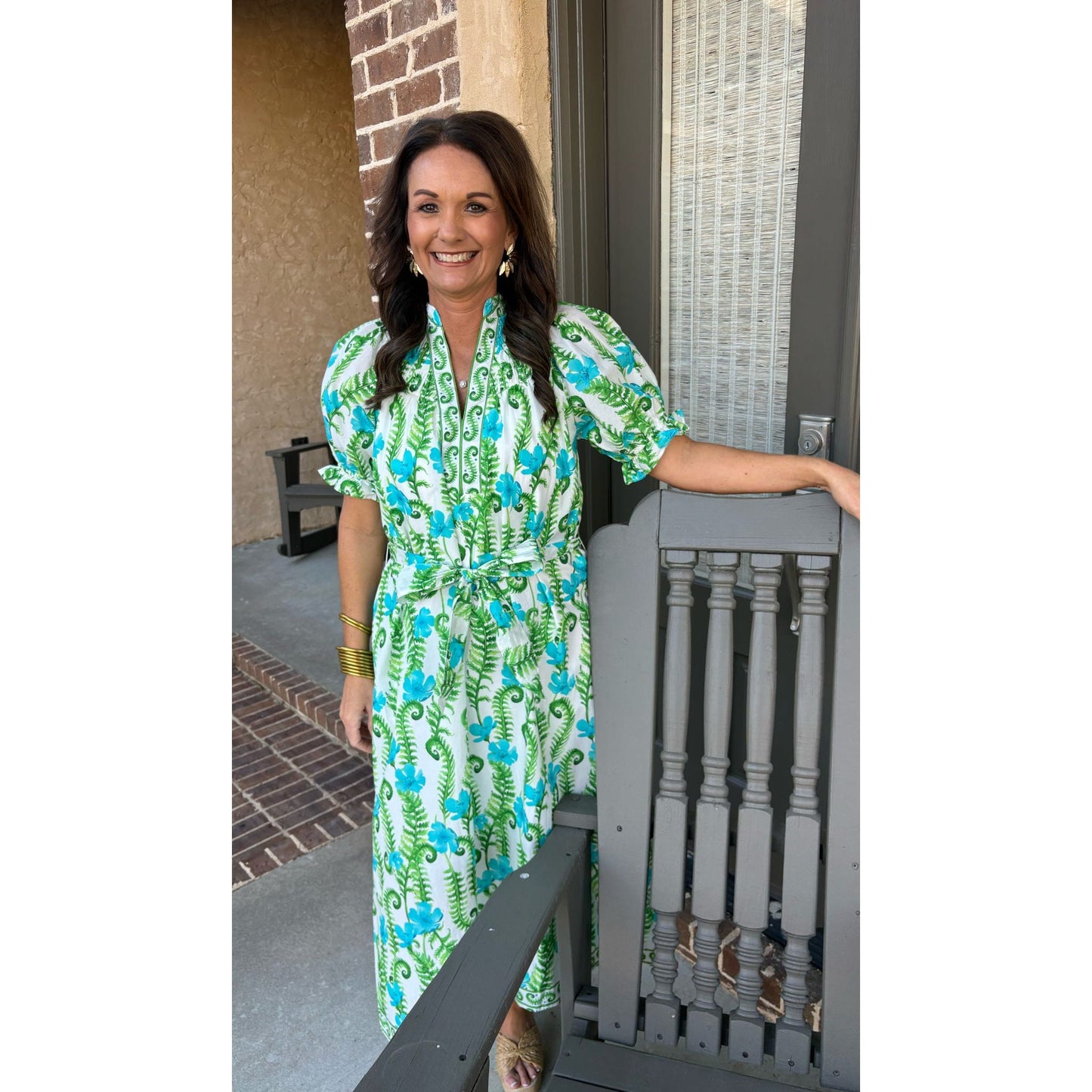 Woman in a green and blue floral dress standing on a porch.