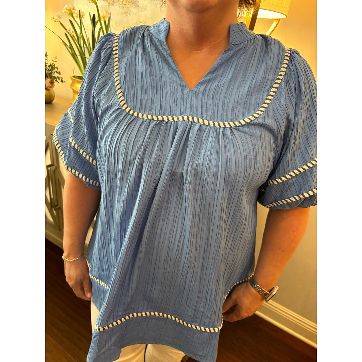 Person wearing a blue striped shirt with decorative trim indoors.