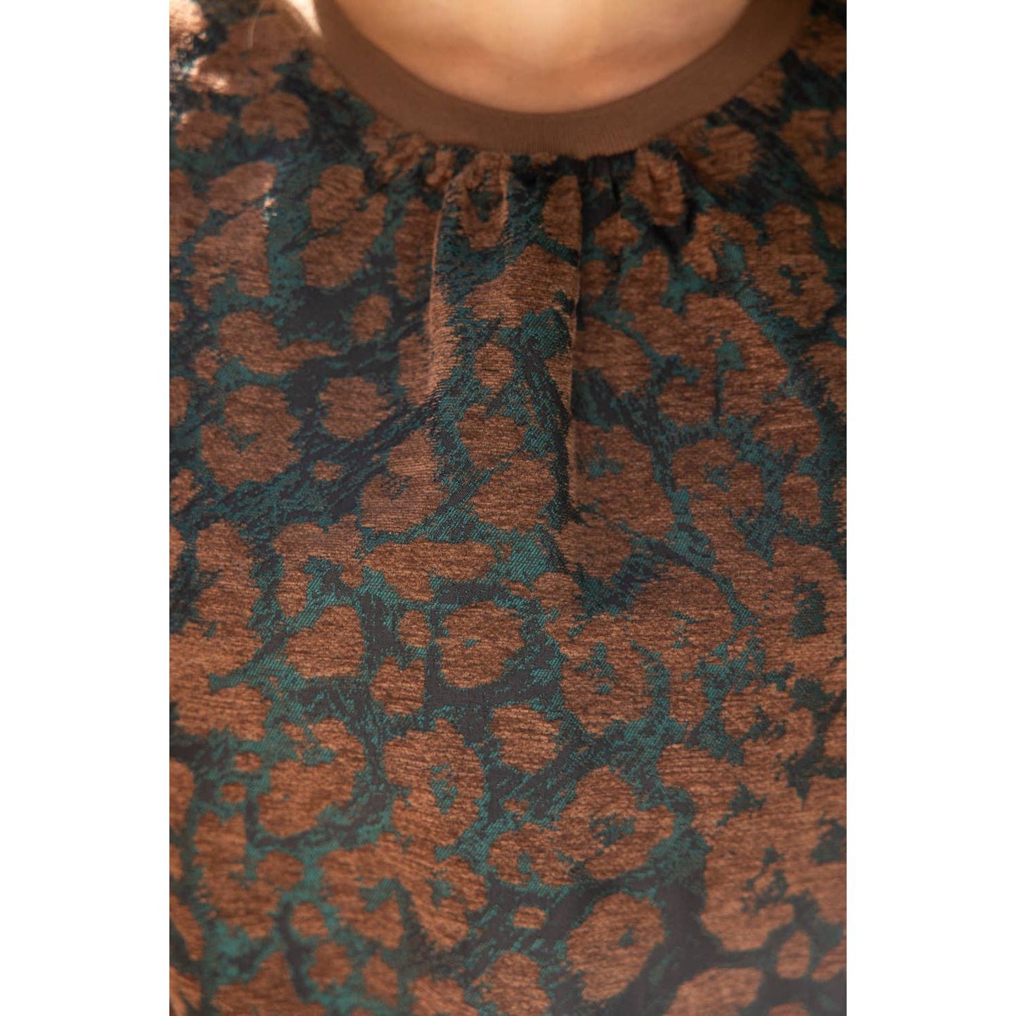 Close-up of a textured fabric top with an abstract leopard-like pattern in dark brown and teal green, featuring a gathered neckline.