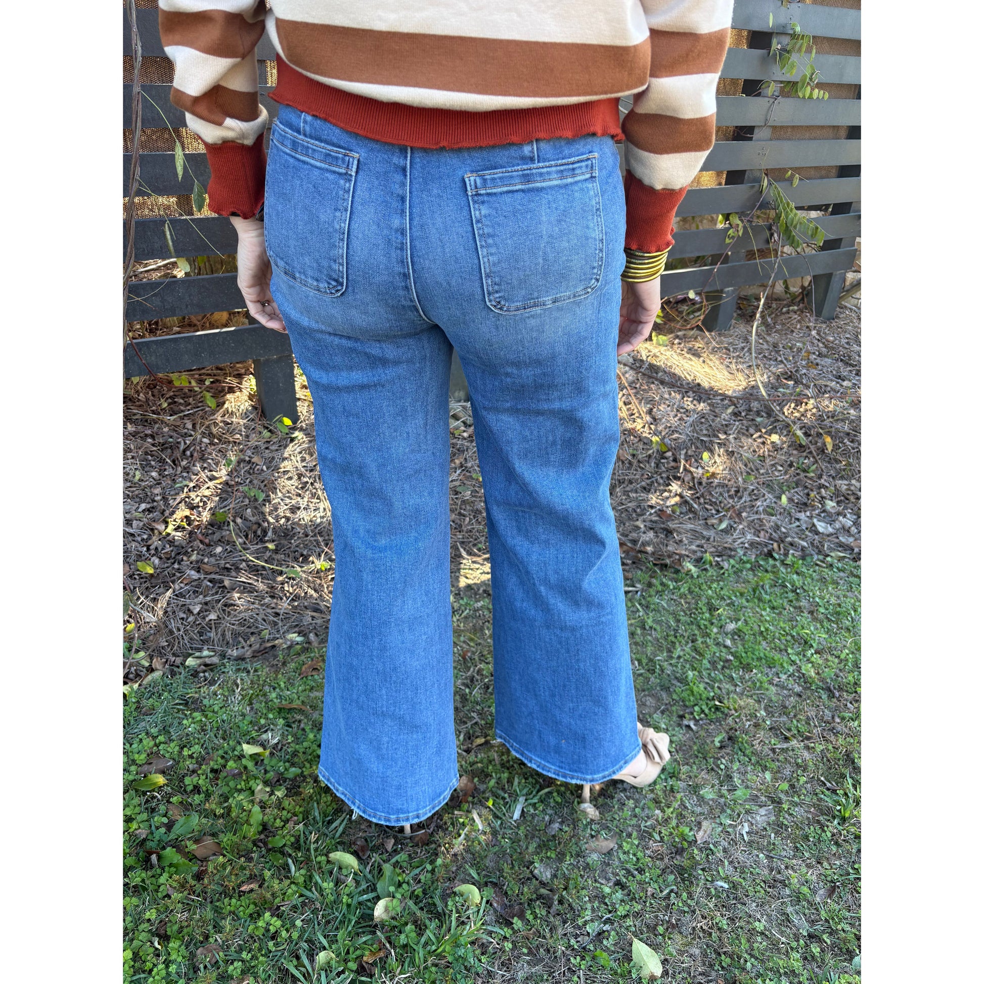 Person wearing blue jeans and a striped shirt on a grassy ground.