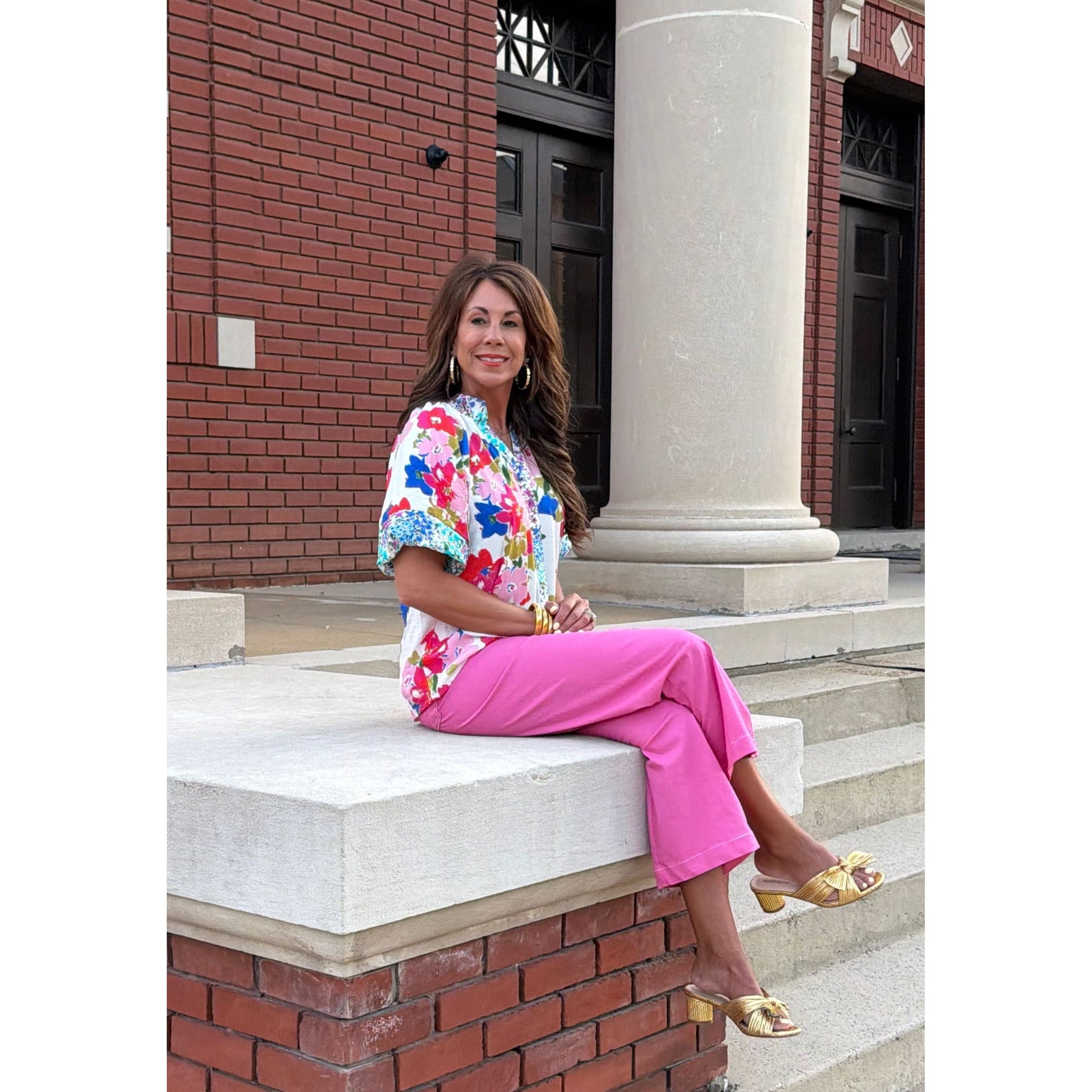 Woman in a colorful dress and pink skirt sitting on steps with a building in the background