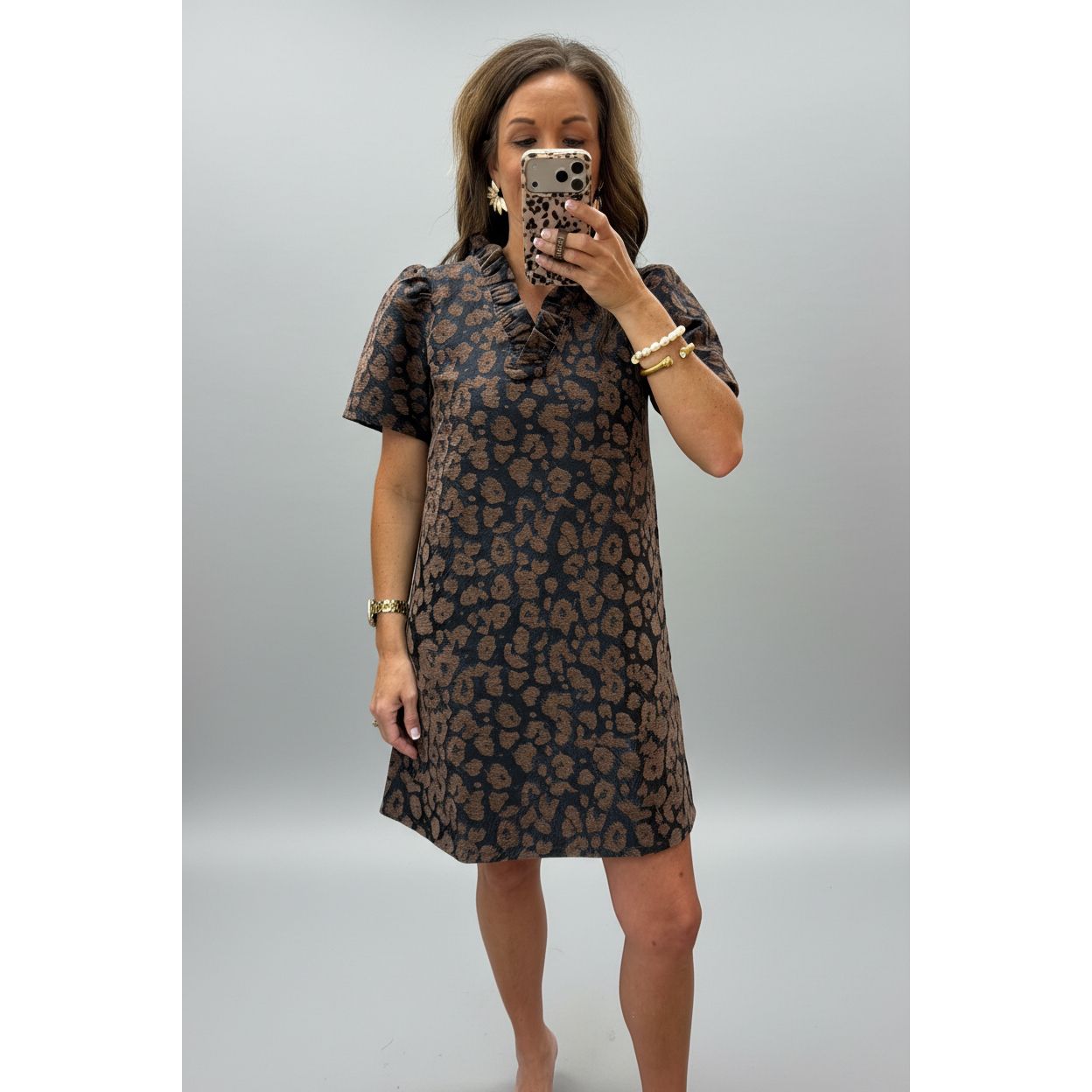 A woman takes a mirror selfie in a clothing store wearing a short-sleeve shift dress with a brown and black leopard print pattern.
