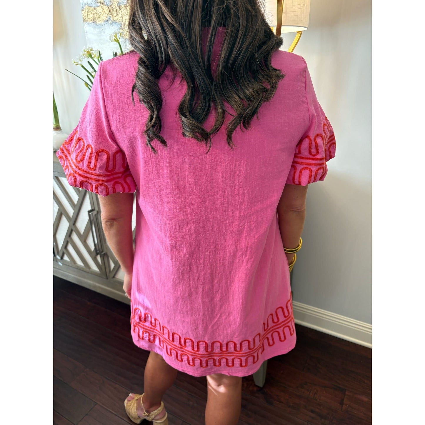Person wearing a pink dress with red patterns in an indoor setting