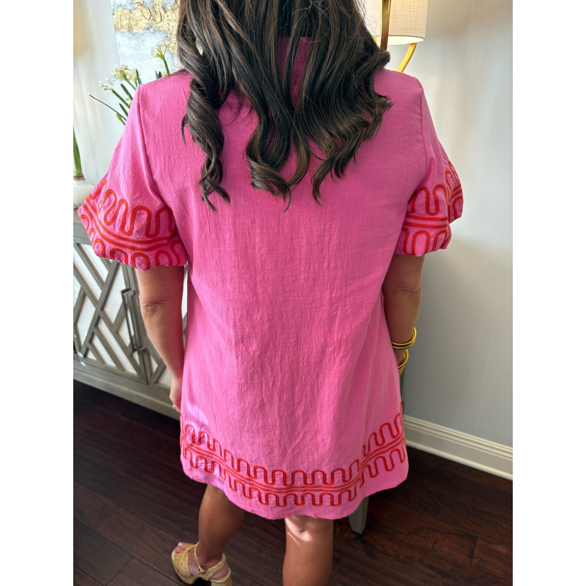 Person wearing a pink dress with red patterns in an indoor setting