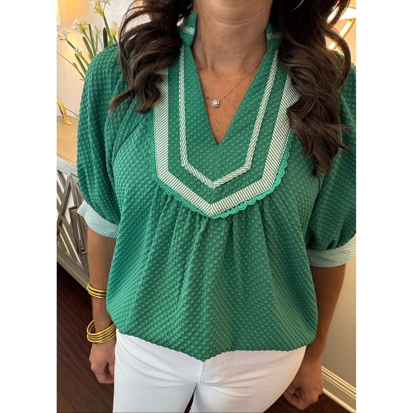 Woman wearing a green blouse with white trim indoors