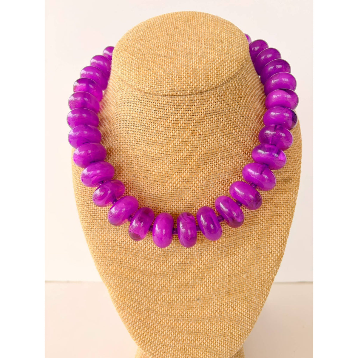 Purple beaded necklace on a mannequin bust against a beige background