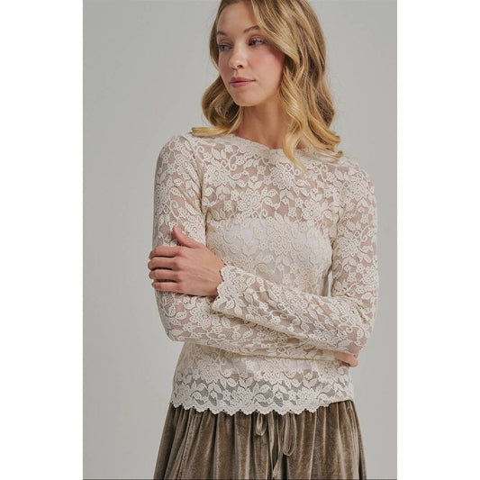A woman wearing a beige lace long-sleeve top with a scalloped hem and a brown velvet skirt, photographed against a neutral light gray studio background.