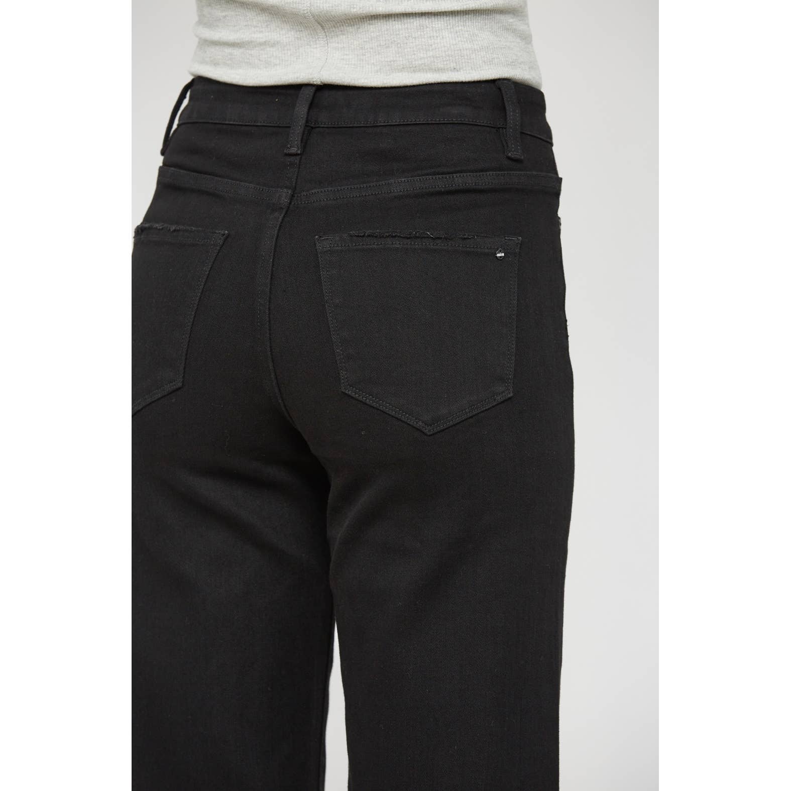 Rear view of a person wearing black denim jeans with a light gray top, cropped from the waist down against a plain light gray background.