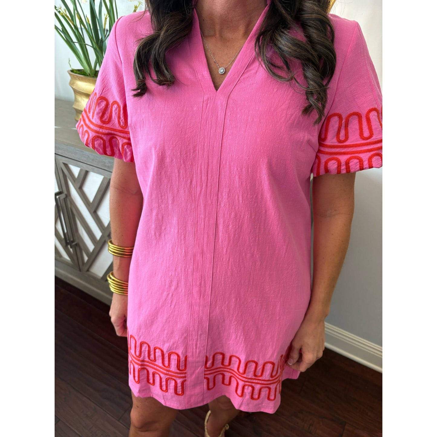 Person wearing a pink dress with red patterns in a home setting