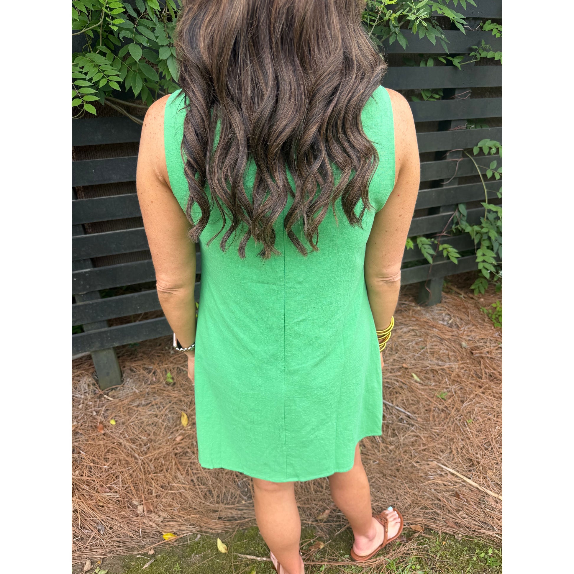 Person wearing a green dress standing outdoors with plants in the background