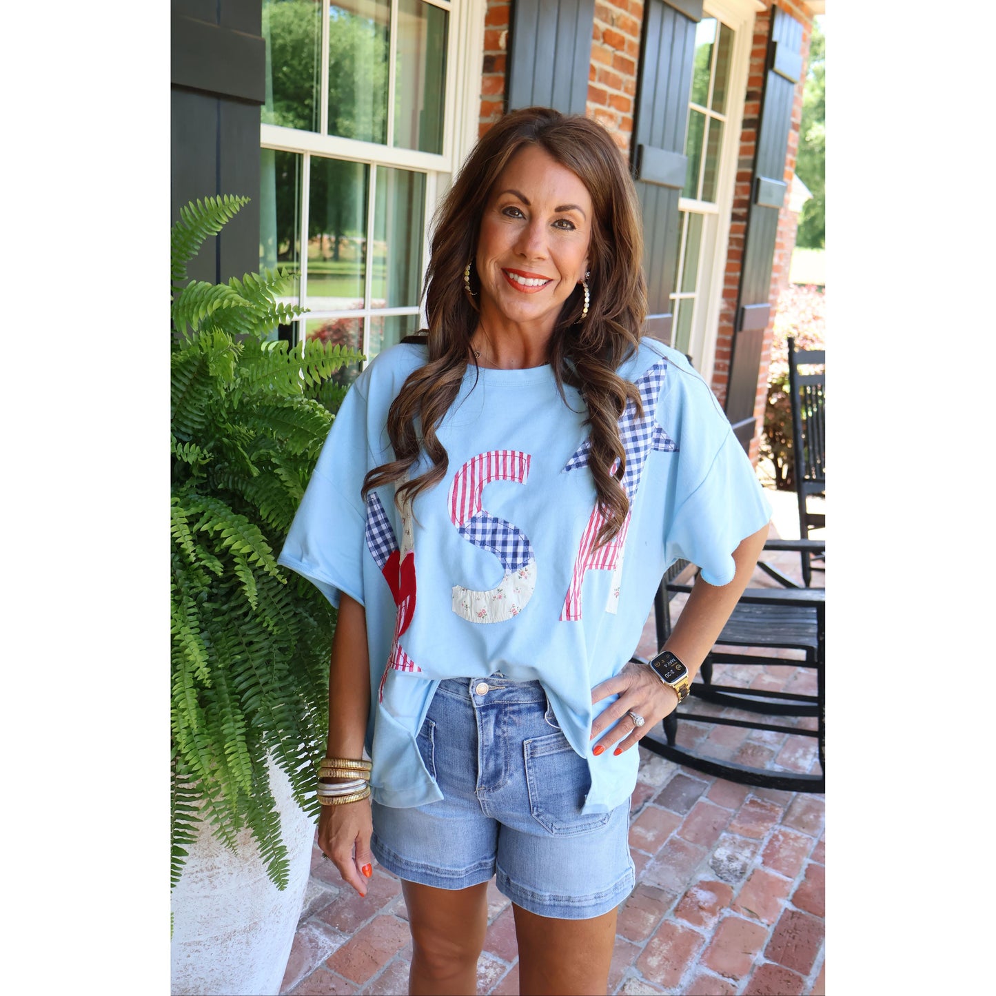 Woman wearing a light blue t-shirt with a graphic design, standing outdoors.