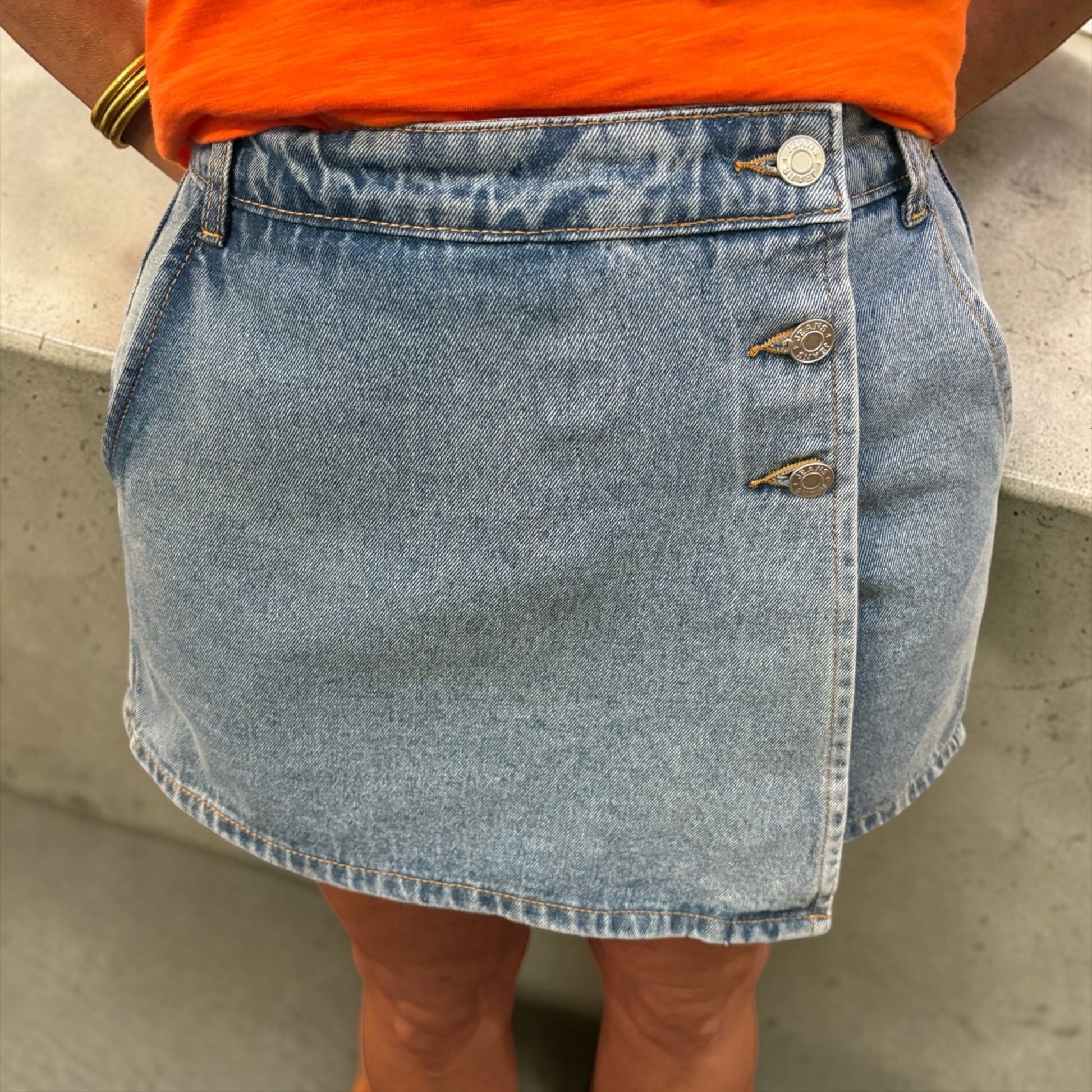 Person wearing a blue denim skirt with an orange top against a neutral background