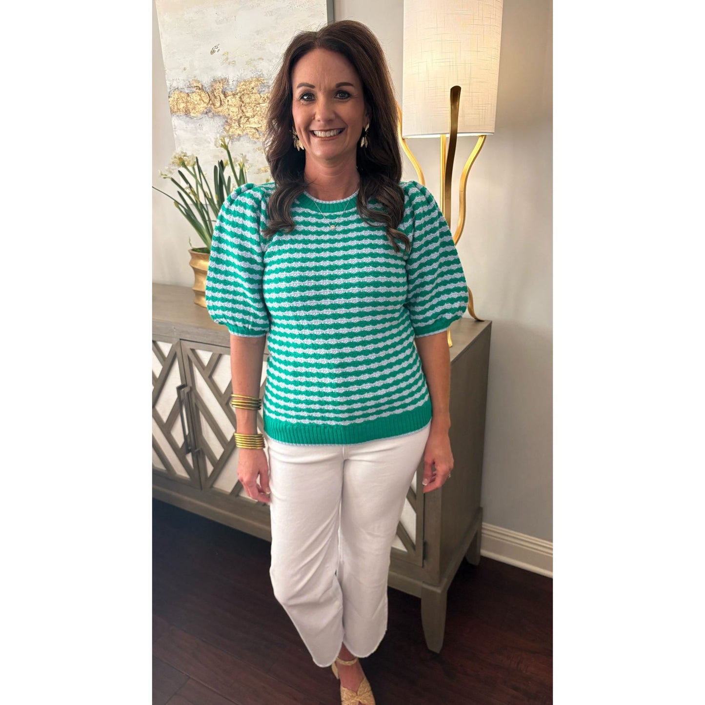 Woman wearing a green and white striped sweater and white pants indoors.