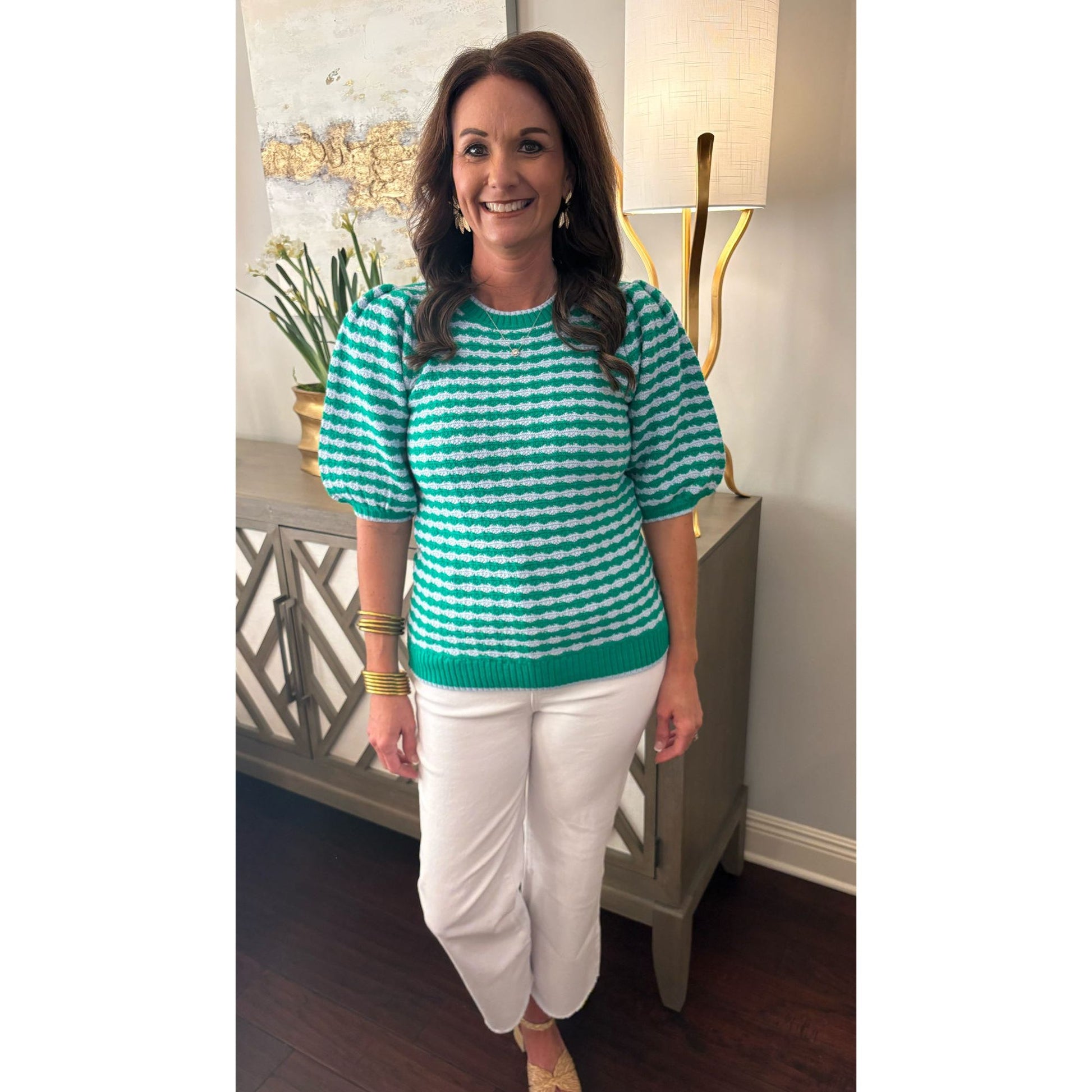 Woman wearing a green and white striped sweater and white pants indoors.