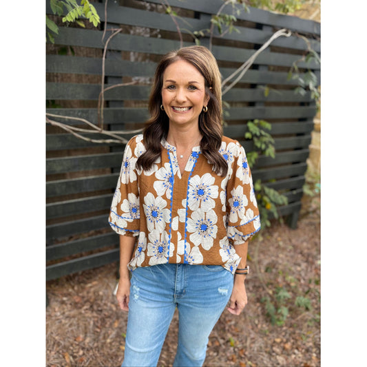 Woman wearing a floral blouse and jeans standing in front of a wooden fence.