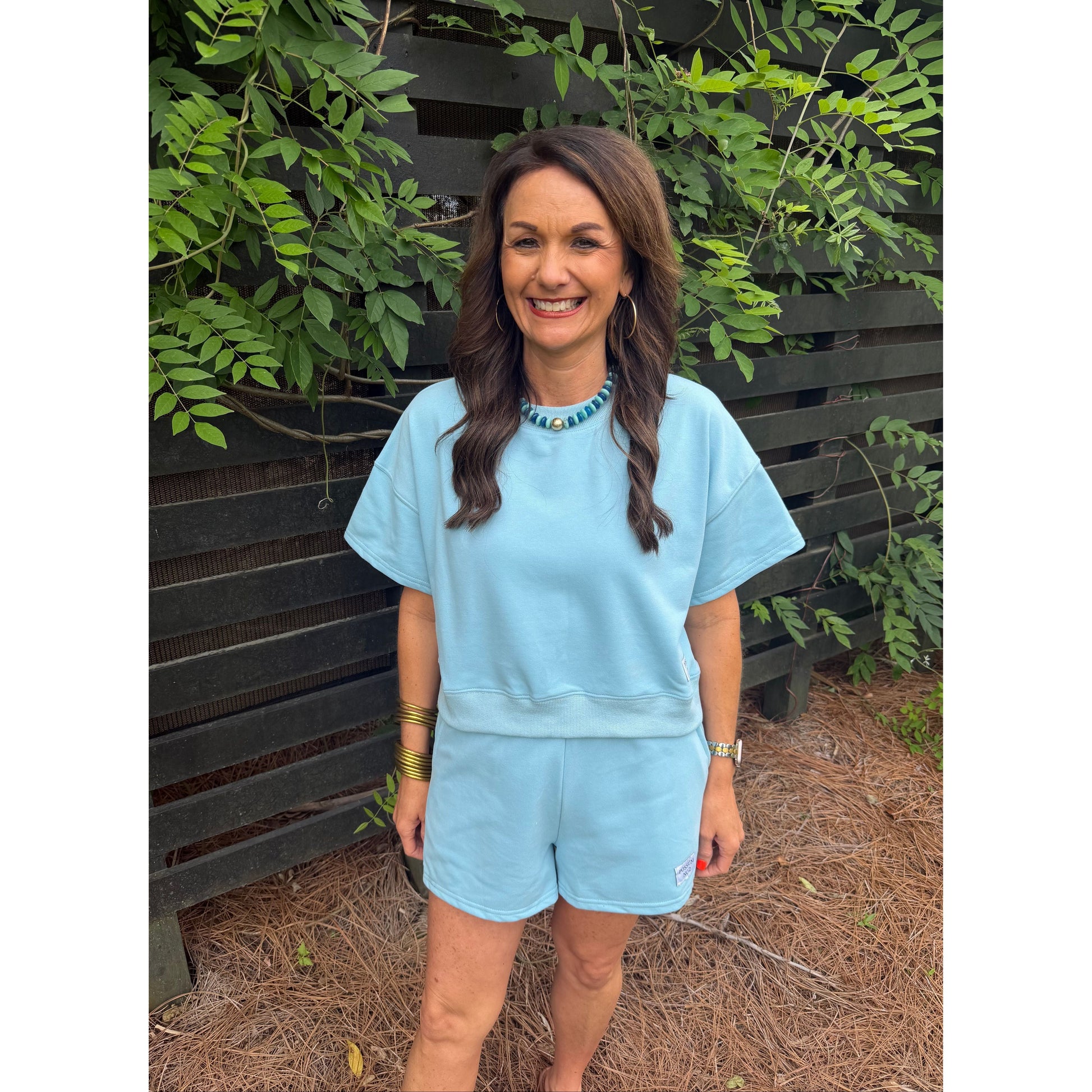 Woman wearing a light blue dress standing outdoors with greenery around.