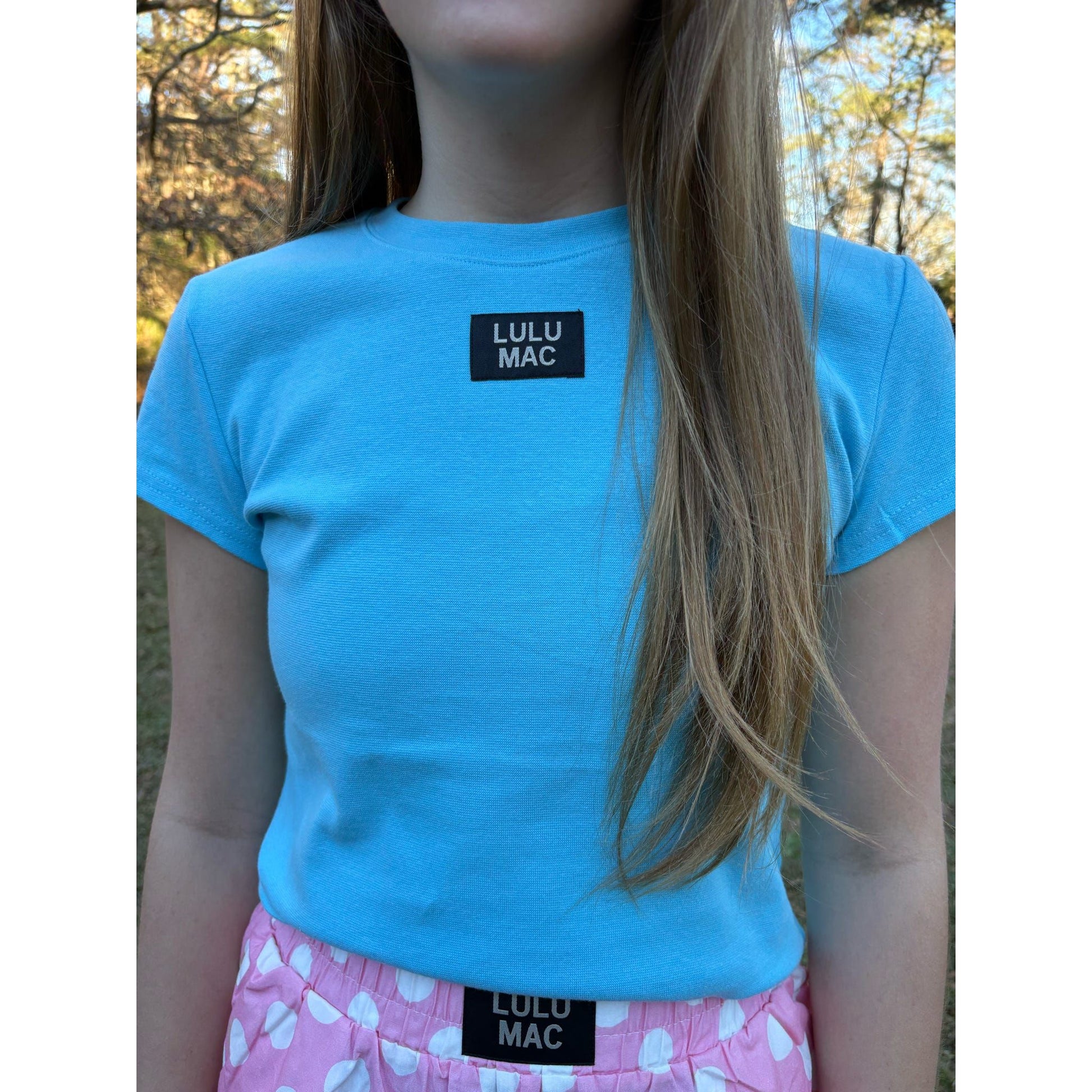 Person wearing a blue LULU MAC t-shirt with a blurred outdoor background