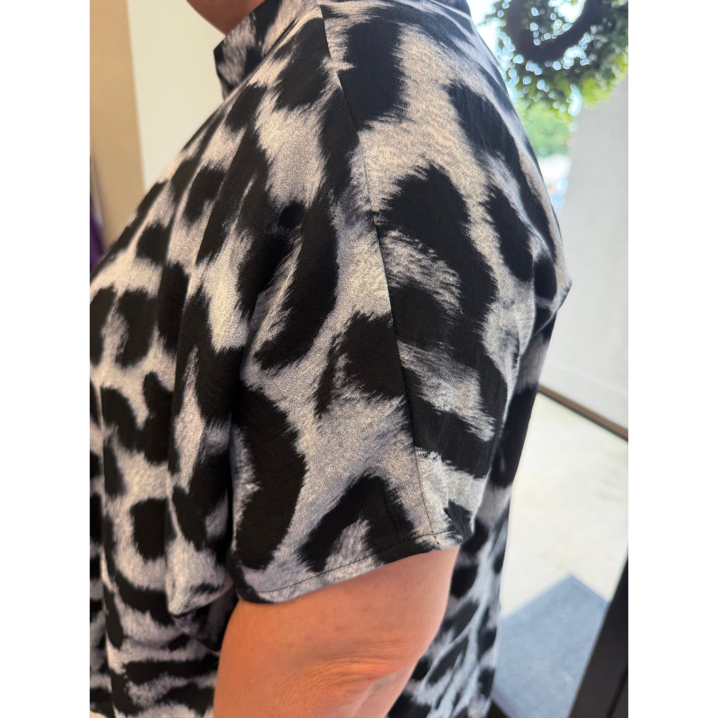 Close-up of a person wearing a short-sleeve top with a black and gray leopard print pattern, showing the side and back of the garment.