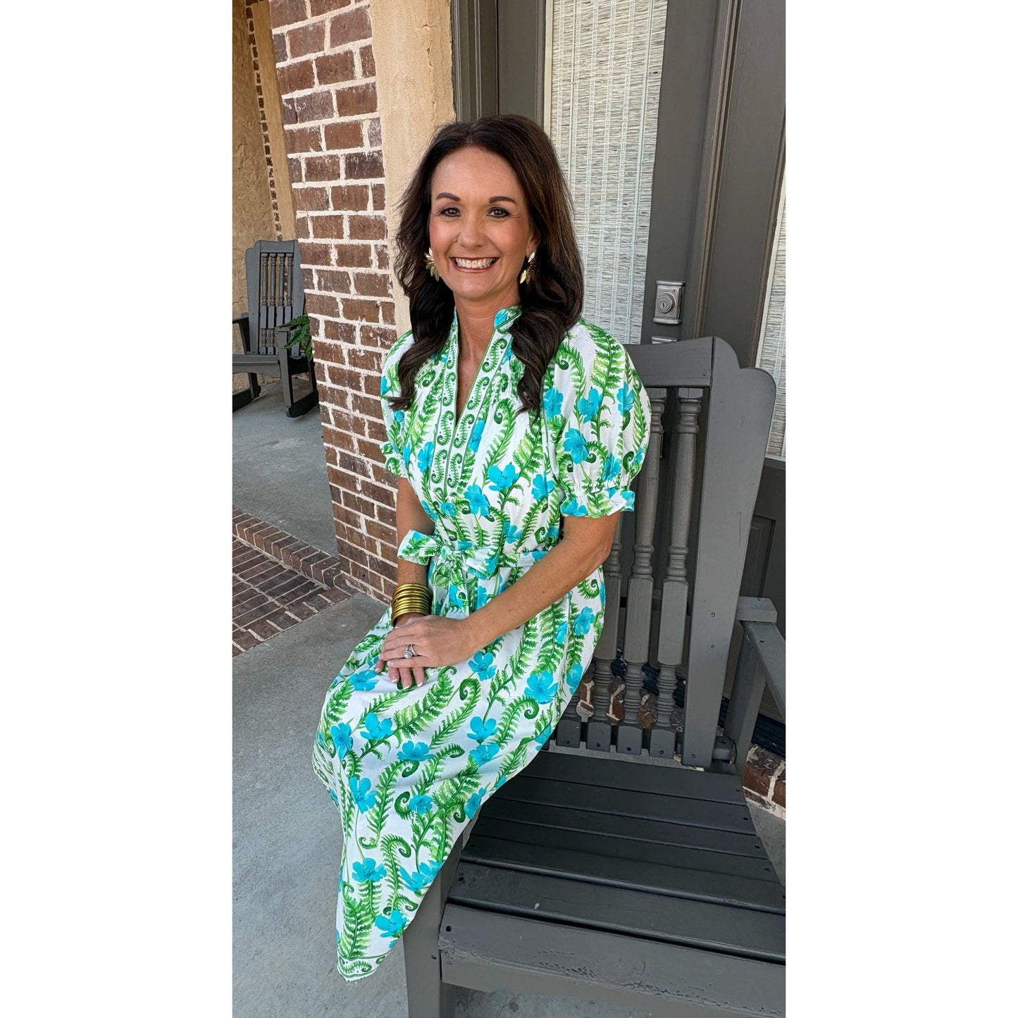 Woman in a green and blue patterned dress sitting on a porch.
